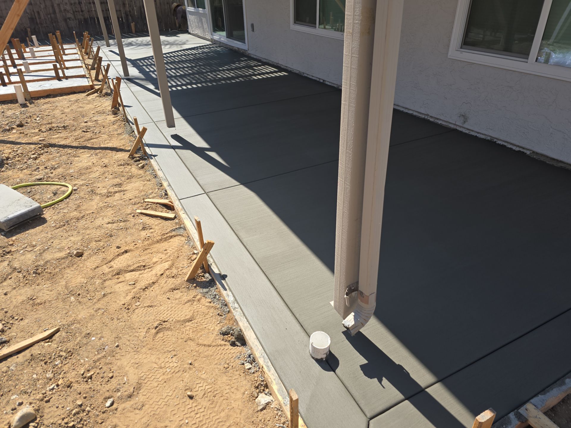 Newly poured concrete patio next to a house under construction. Brown earth surrounds it.