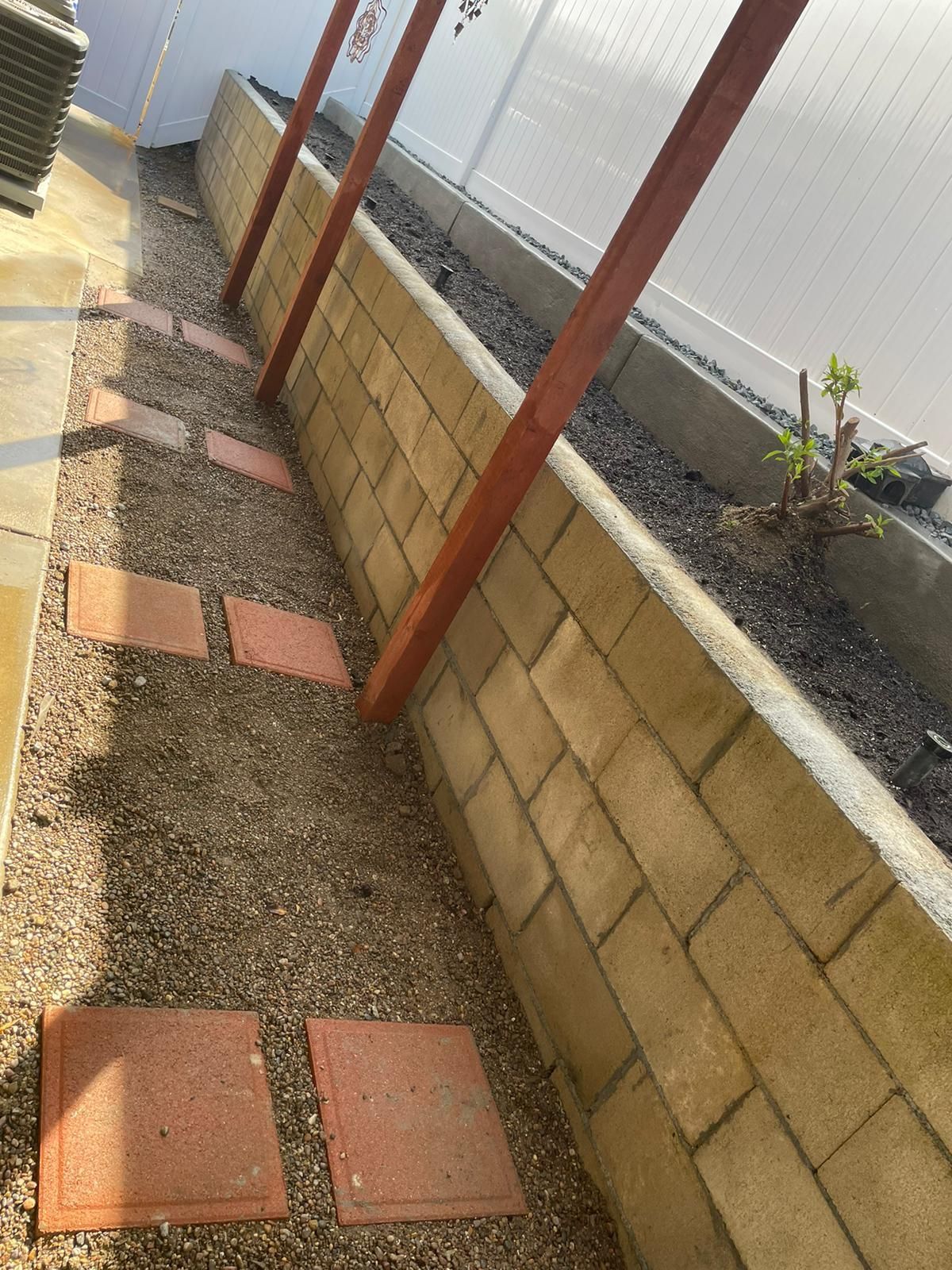 Brick retaining wall with gravel path and stepping stones. Wooden supports for a roof or awning.