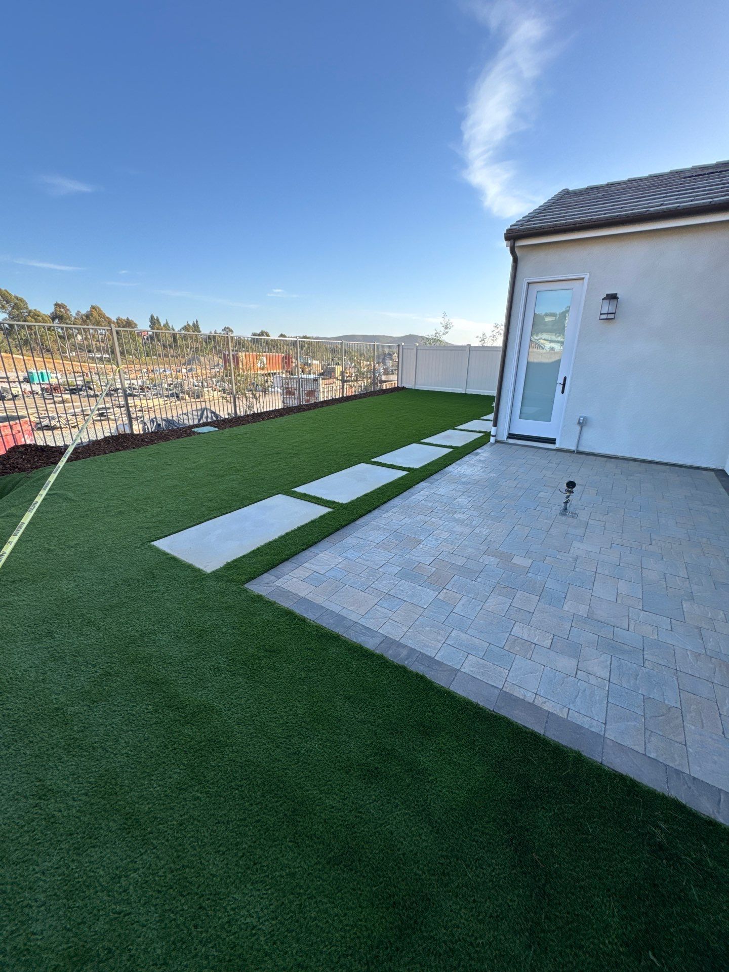 Green turf and stone pavers on a rooftop patio with city views, under a blue sky.