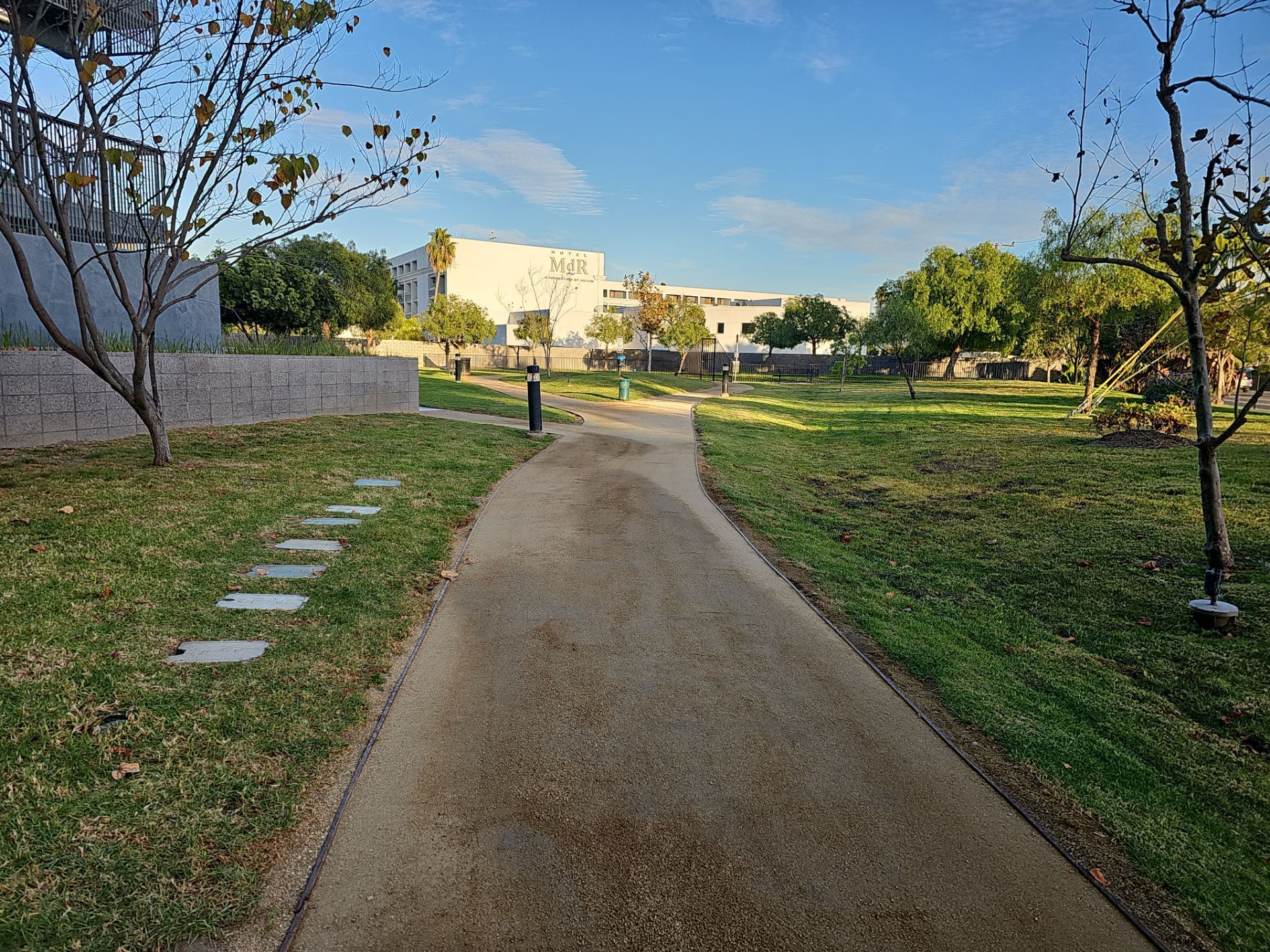 A concrete path winds through a grassy park toward buildings on a sunny day.