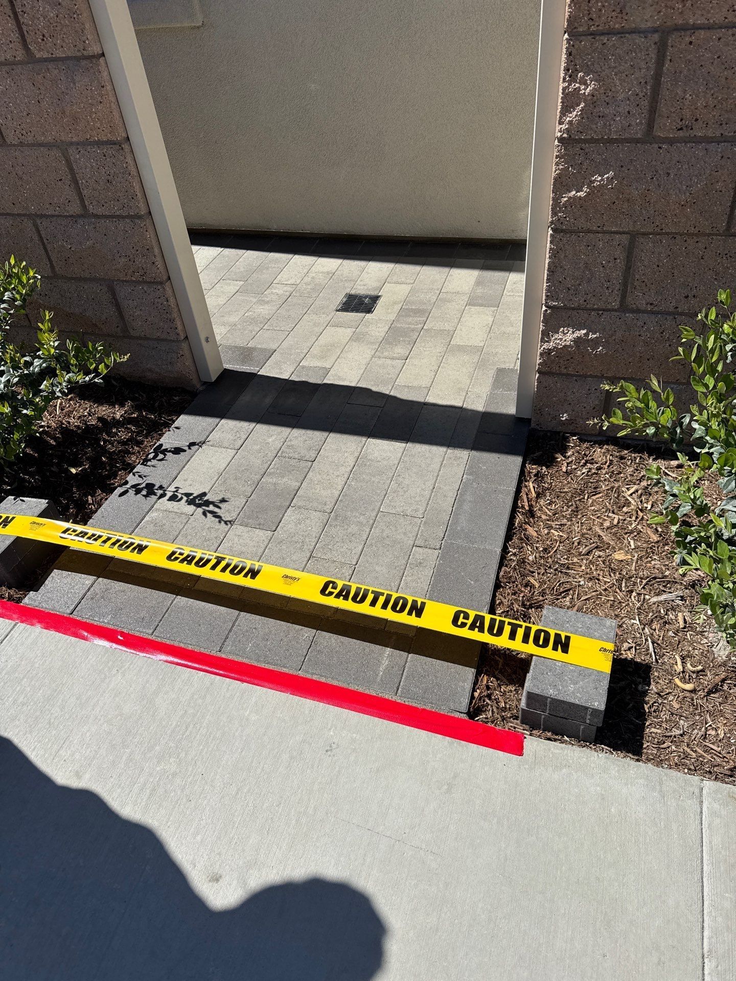 Entranceway blocked by caution tape and red strip, leading to brick pathway.