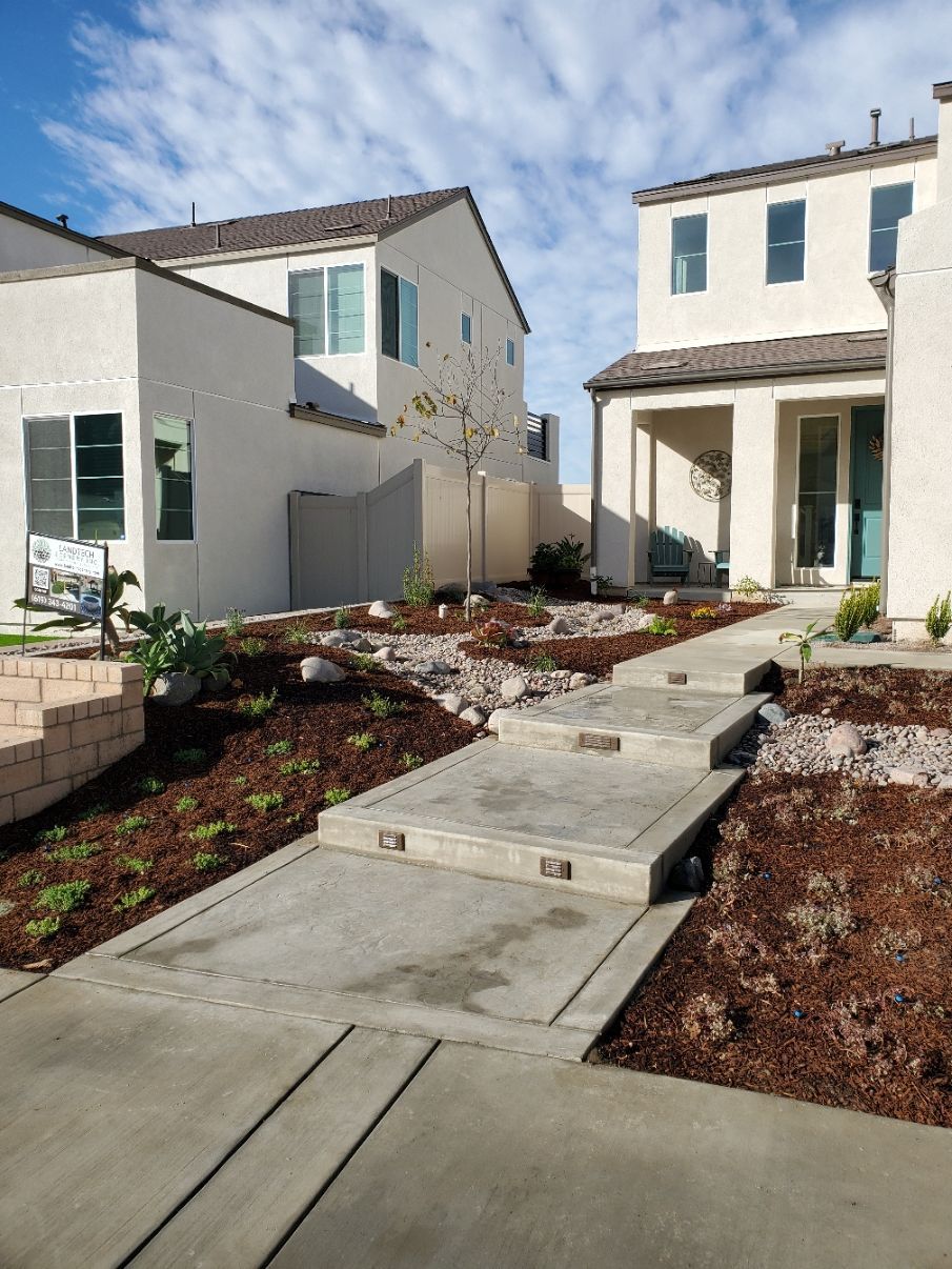 Concrete steps lead to a house entrance. A garden with brown mulch and small plants is beside the steps.