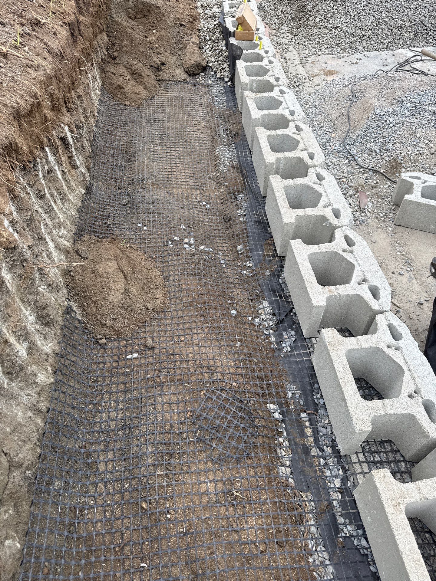 Construction site: trench lined with wire mesh and gravel, with a row of concrete blocks.