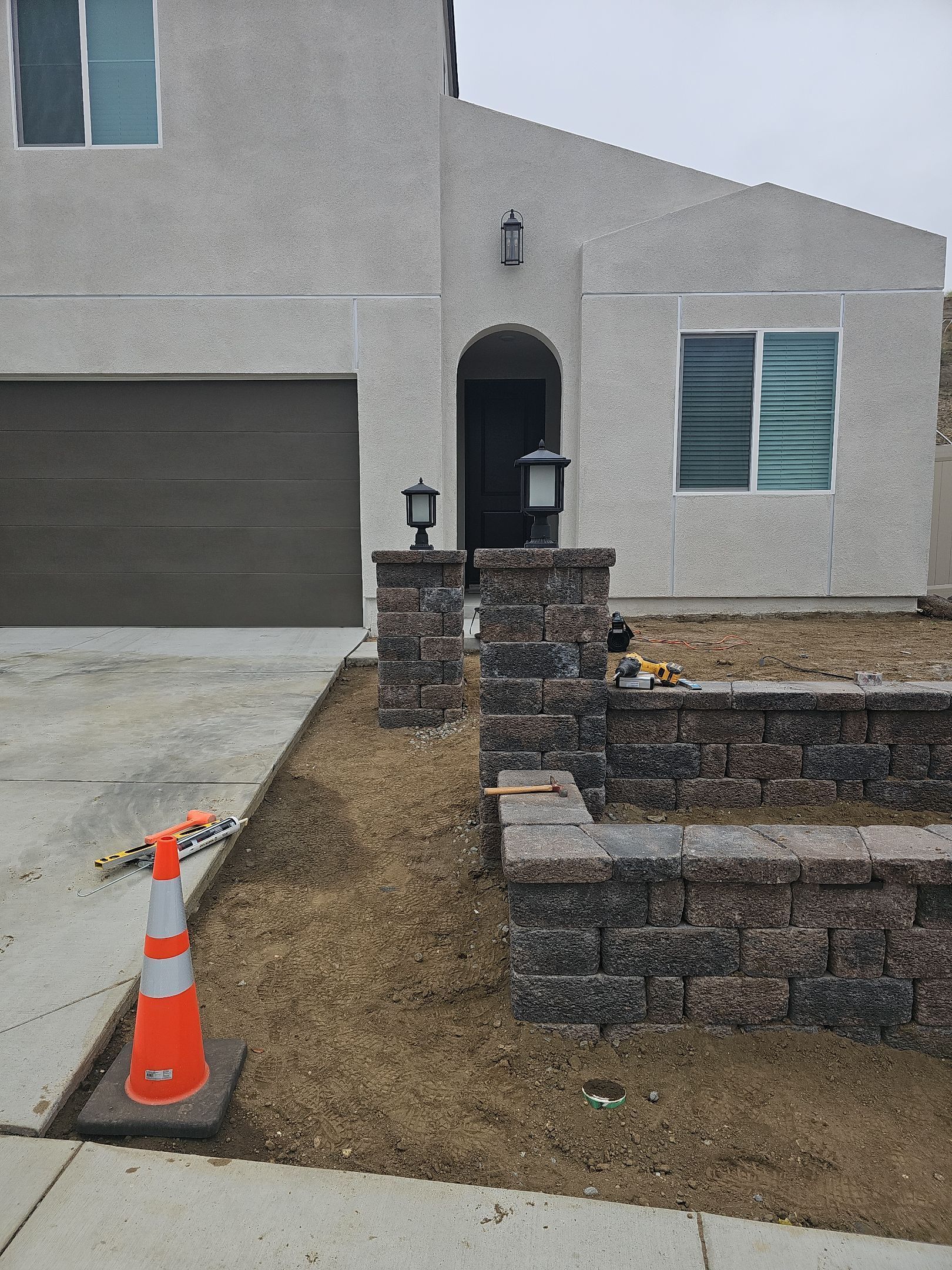 Exterior view of a house with a brown garage door, landscaping and a small retaining wall made of brick.