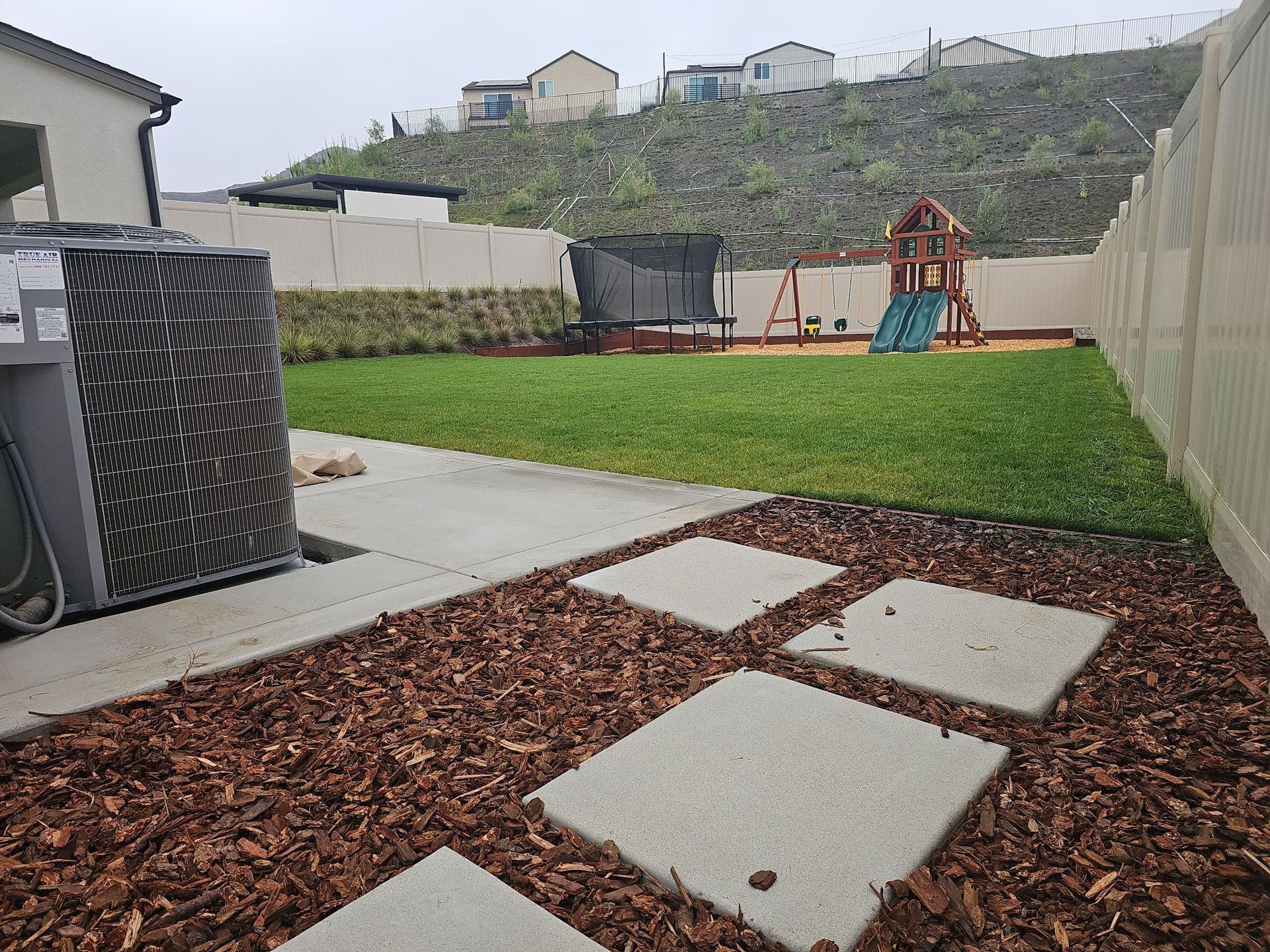 Backyard with a lawn, playground, and paved walkway with stepping stones.