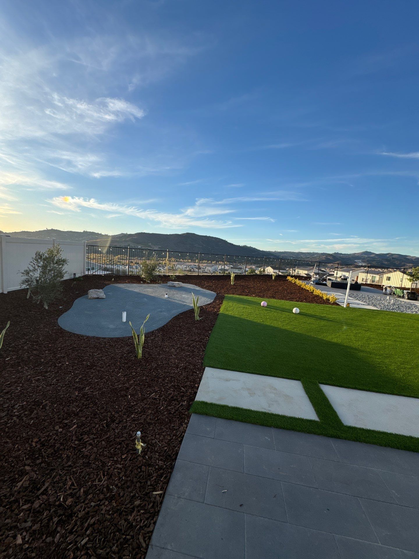 Rooftop landscape with green grass, rock bed, and views of distant hills under a blue sky.