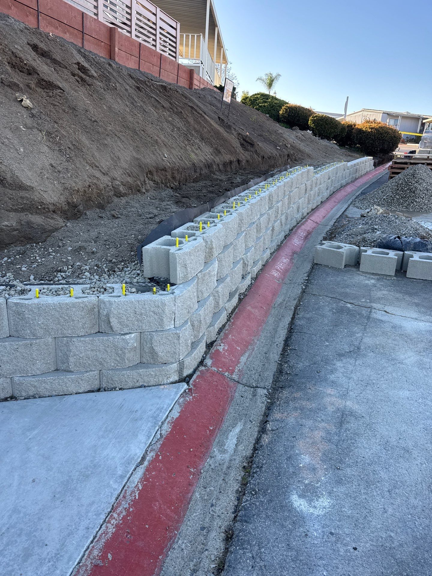 Retaining wall made of concrete blocks, beside a red-lined pathway and dirt hillside.