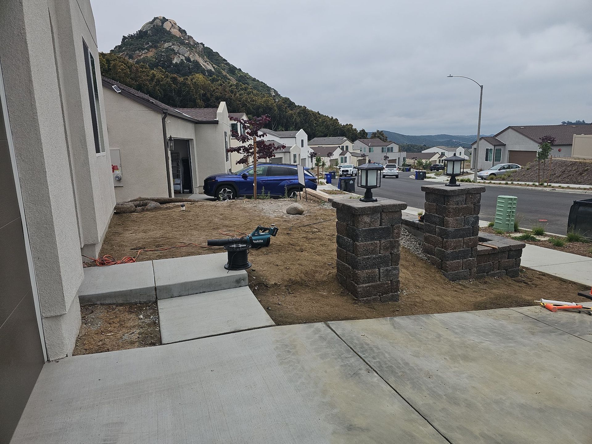 House exterior with stone pillars, lamps, and a mountain backdrop; overcast day.
