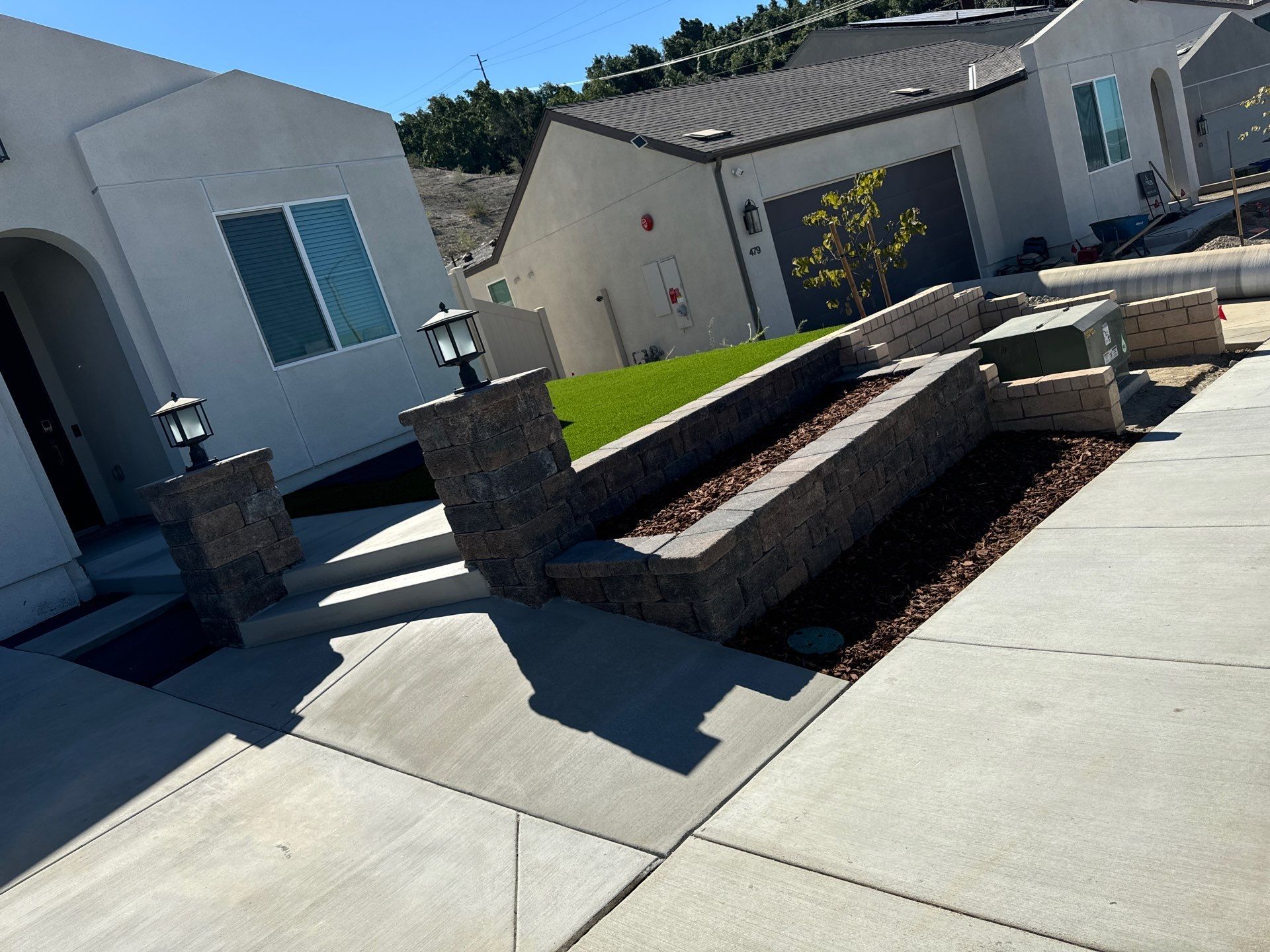 Gray stone steps and walls lead to a house with a green lawn and brown mulch.