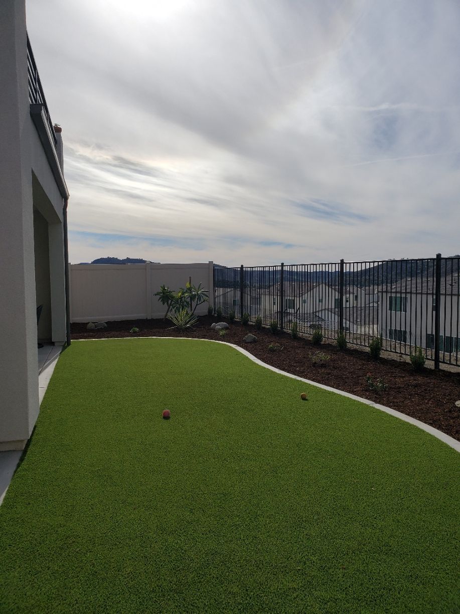 Backyard with artificial grass, a fence, and distant mountains under a cloudy sky.