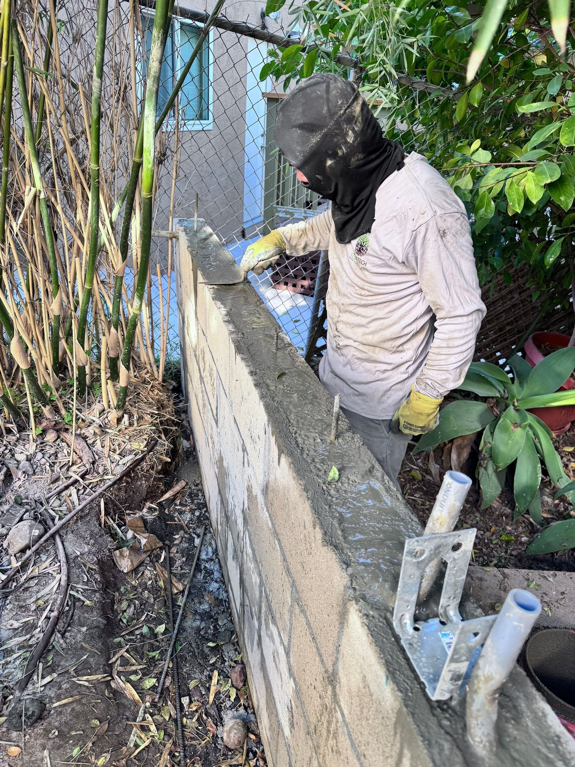 Person in protective gear applying cement to a wall outdoors.
