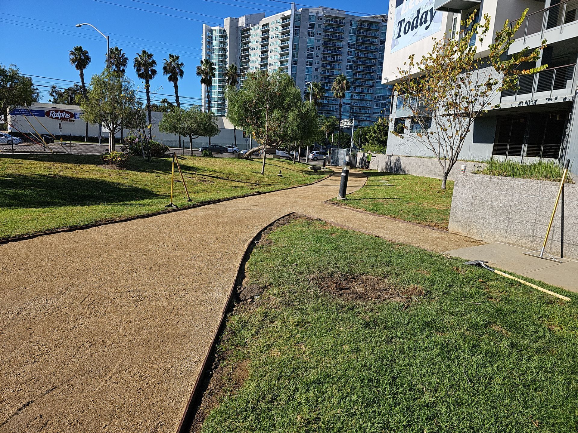 Pathway in park with grass and buildings in the background on a sunny day.