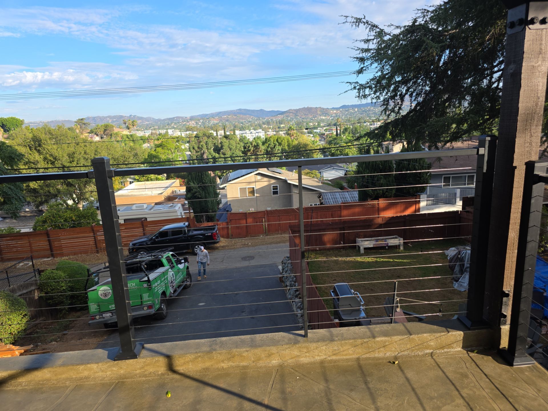 View from a porch overlooking a driveway, yard, and distant cityscape under a blue sky.