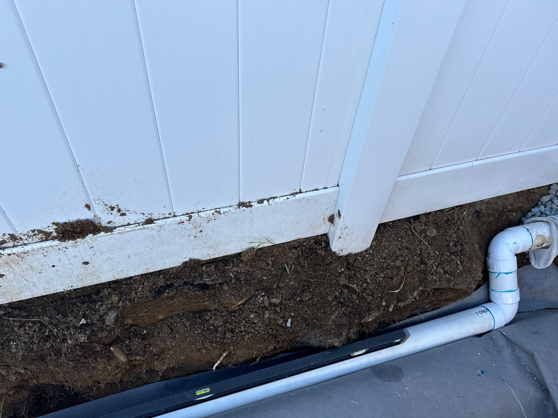 White fence with a PVC pipe and a level on the ground.