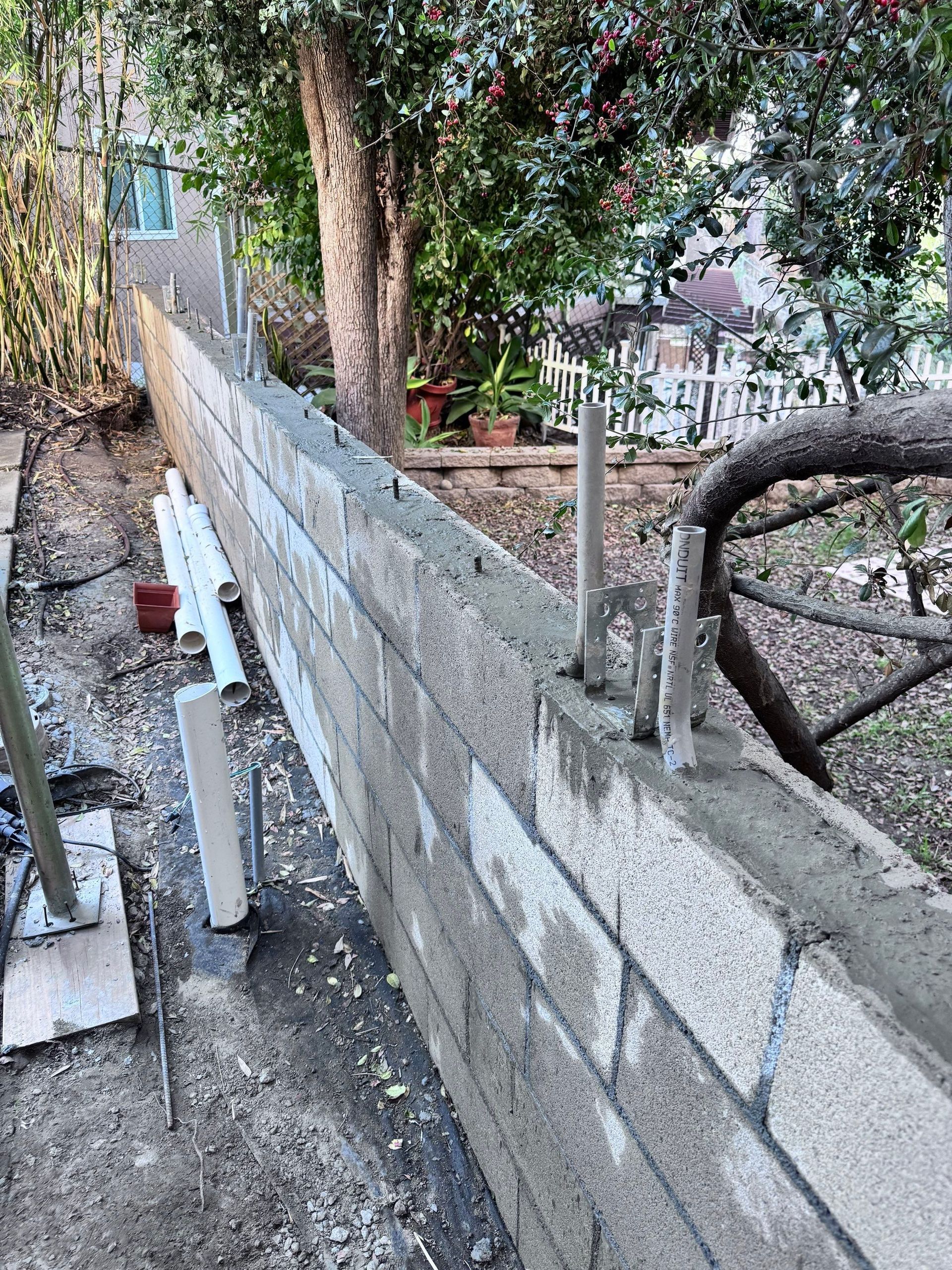 A partially built cinder block wall in an outdoor setting with rebar and mortar visible.