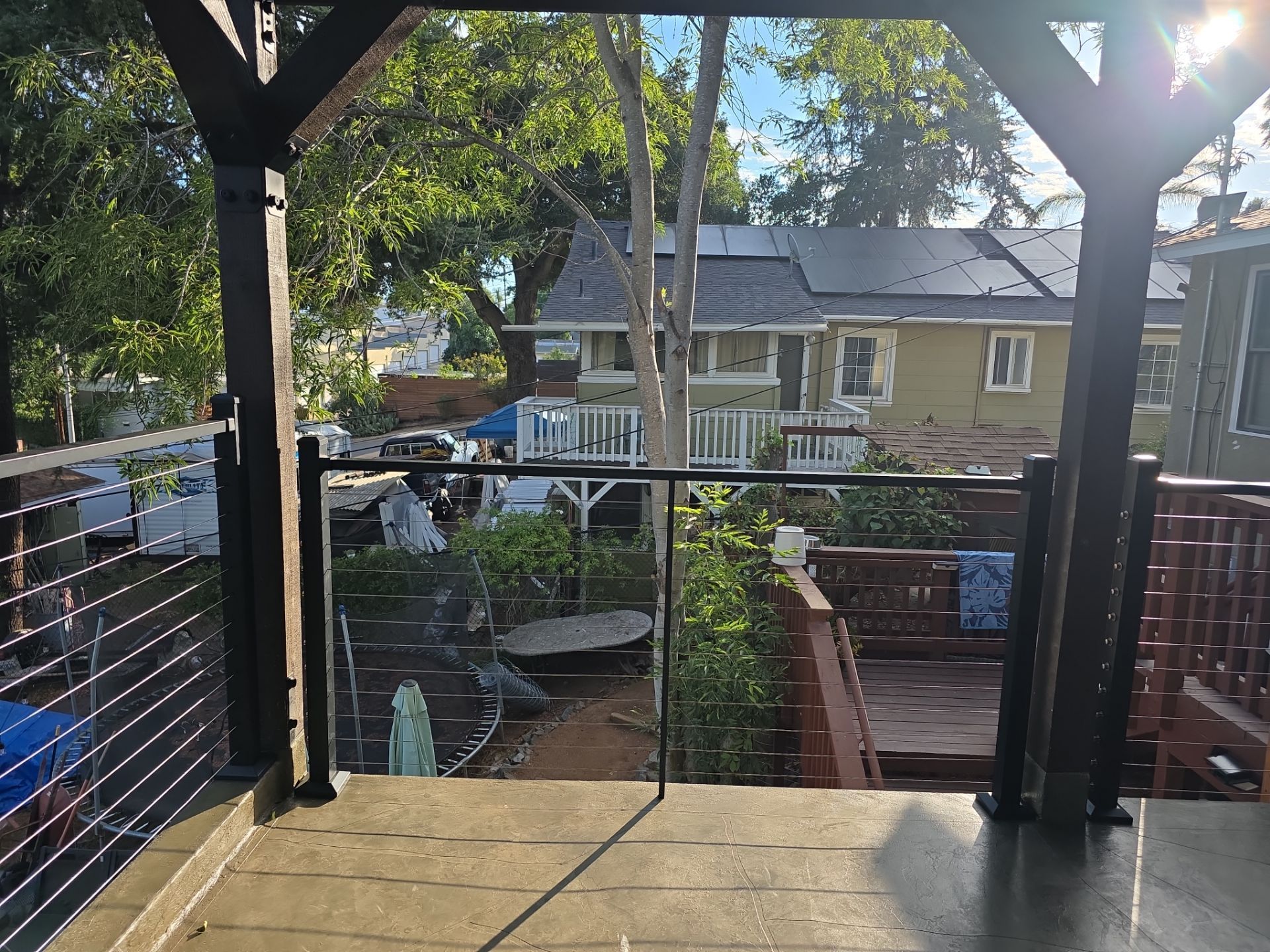 View from a covered porch. A yard with trees, a garden, and houses with solar panels in the background.