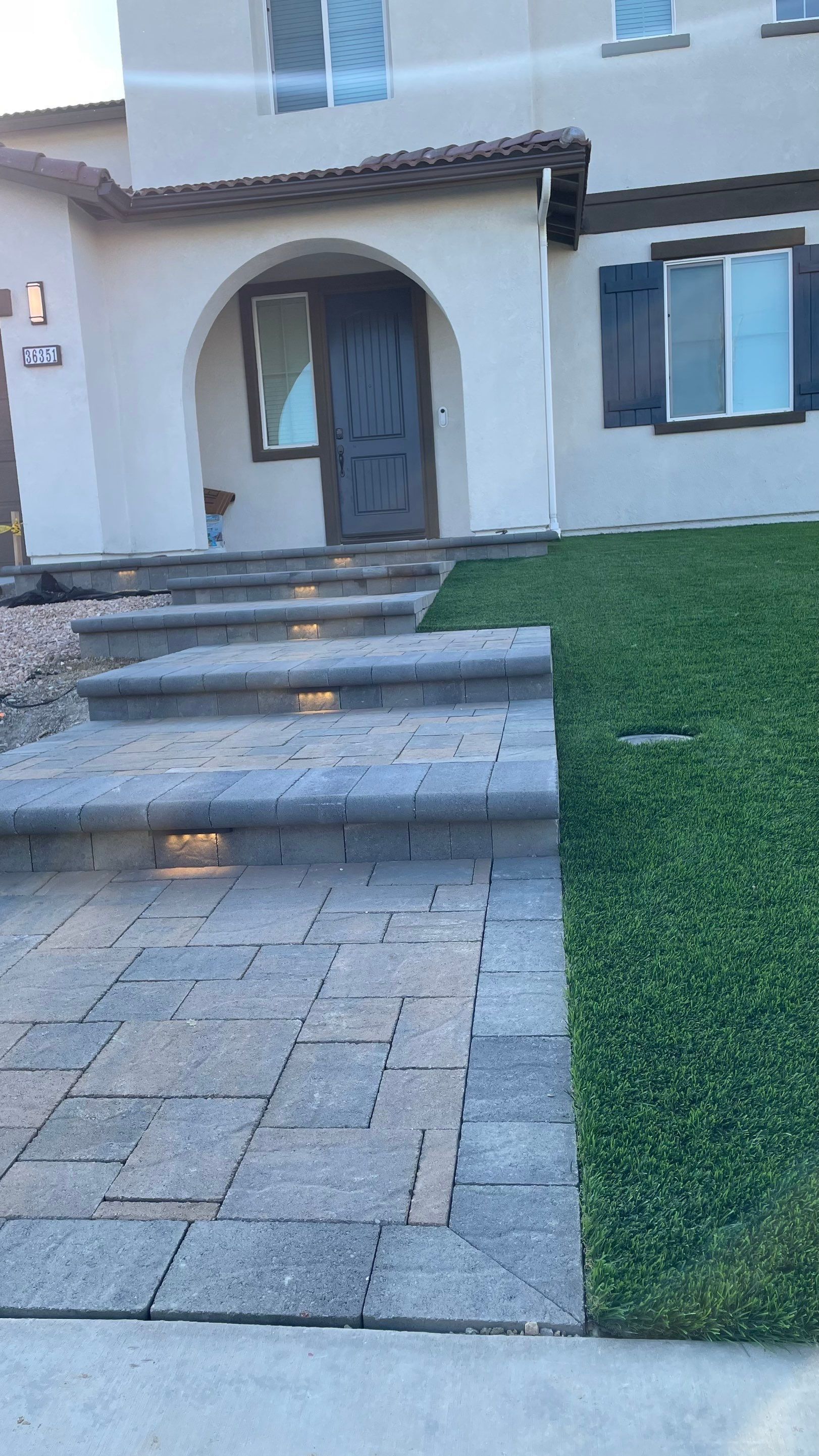 Stone steps and walkway leading to a beige house with a dark wooden door and shutters. Green grass on the side.