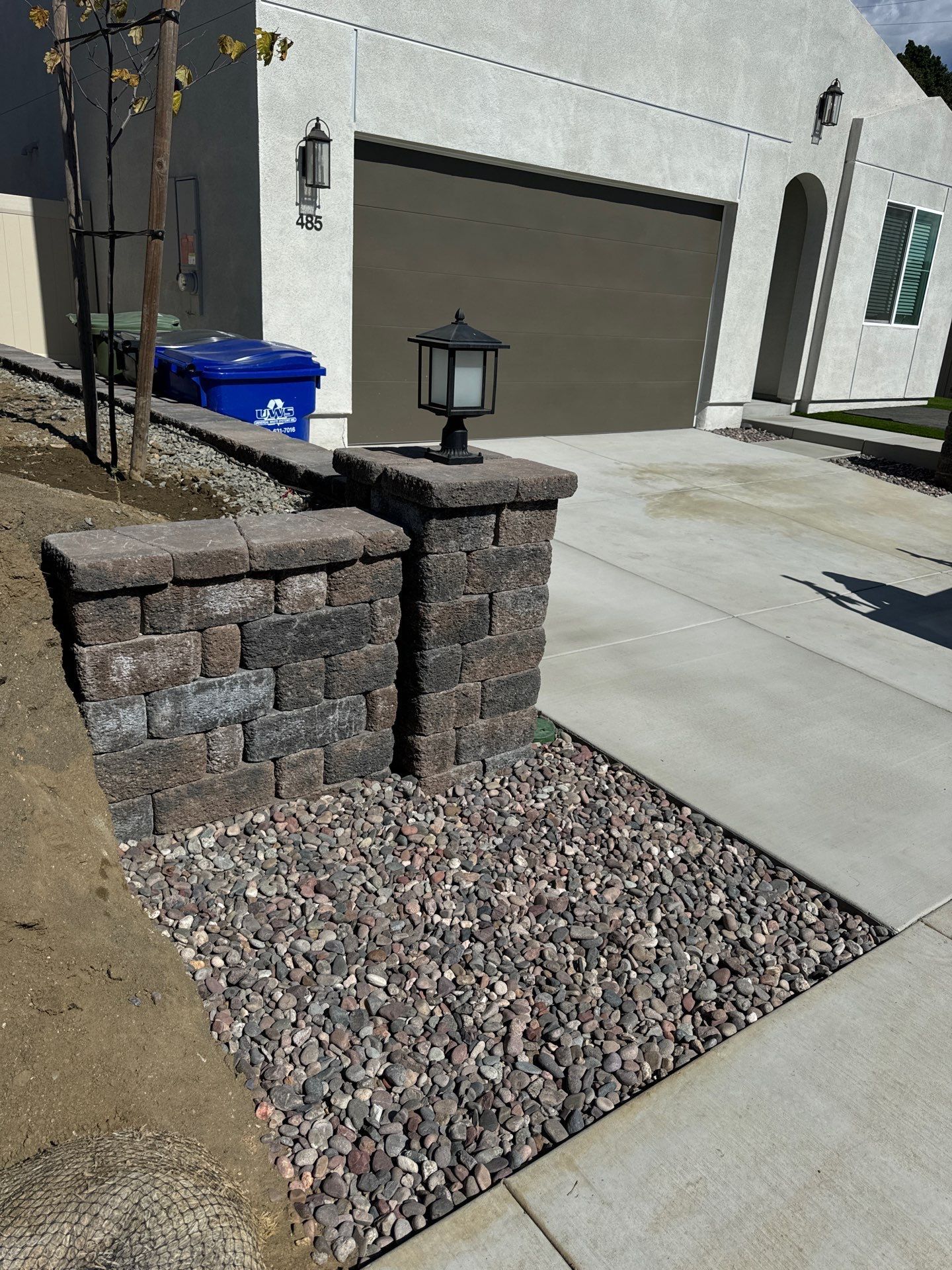 Stone brick pillars with a lantern, gravel bed, driveway, and garage.