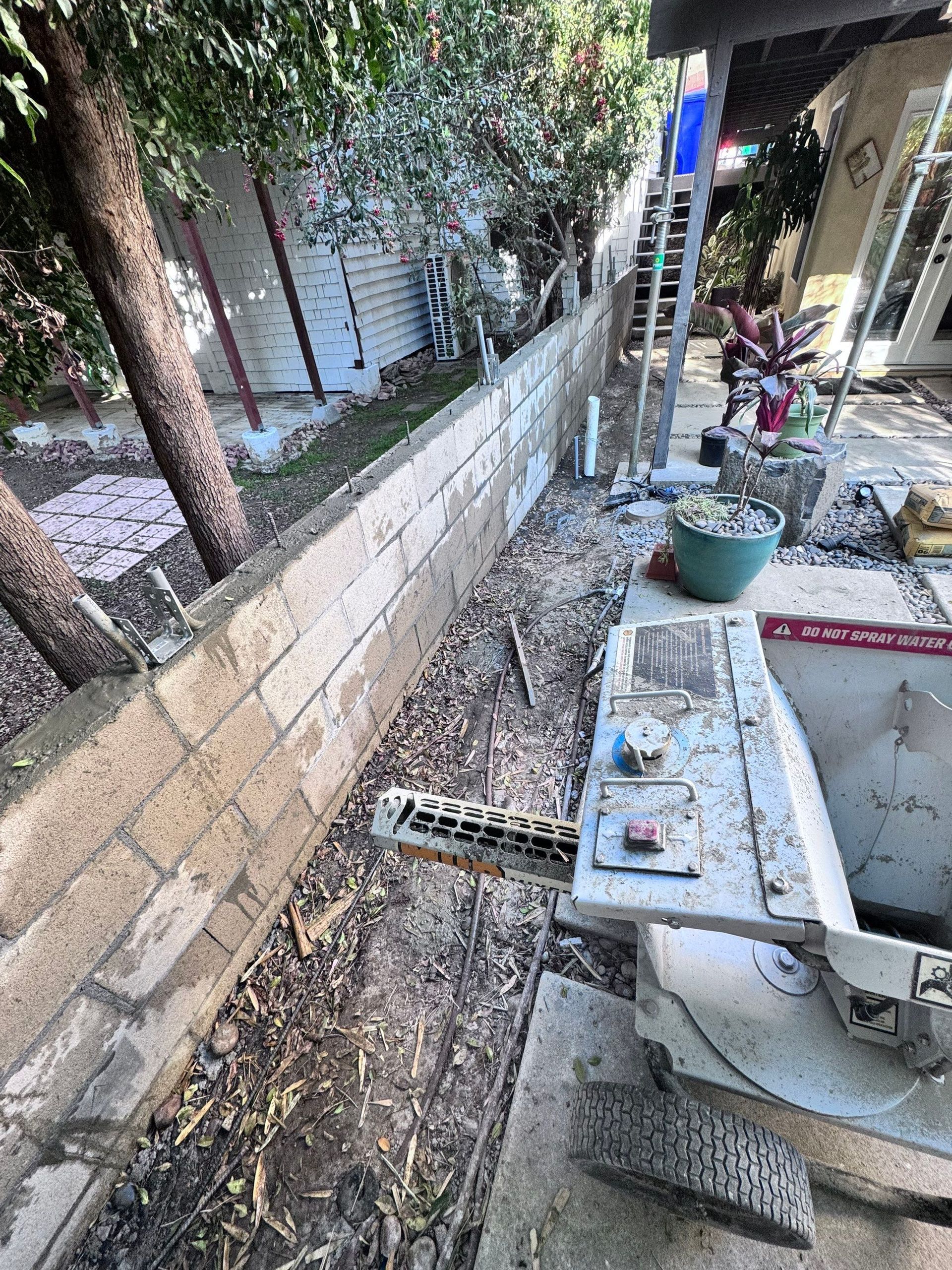 Long, low concrete block wall with debris, next to a concrete surface with machinery.