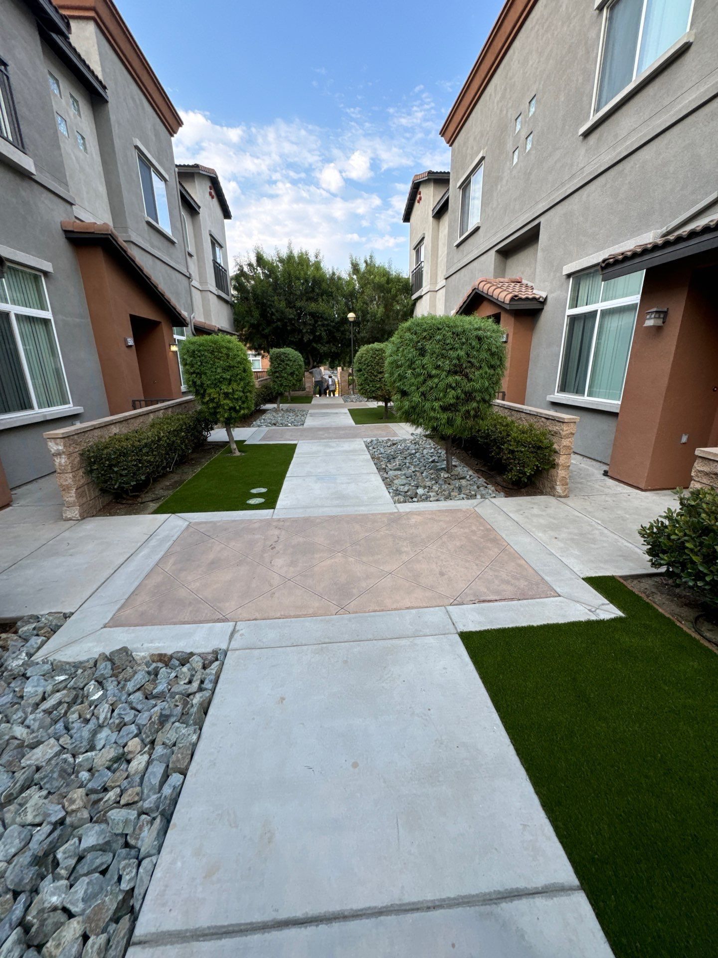 Pathway between townhouses with bushes and rocks.
