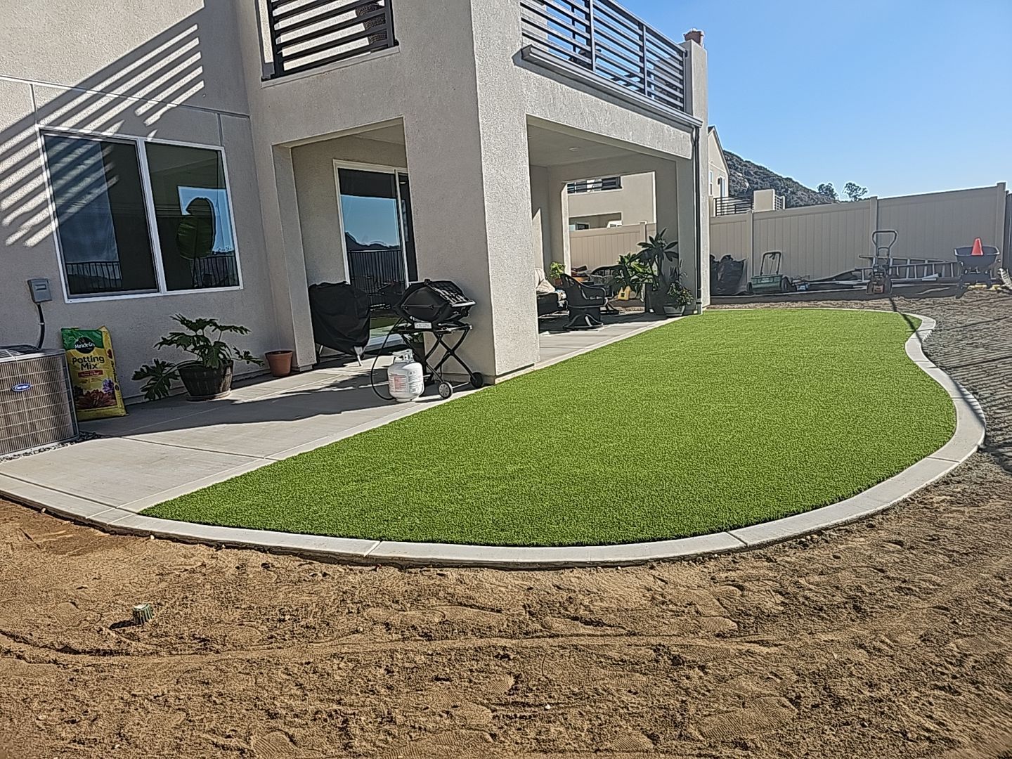 Backyard with green artificial turf next to a house with a concrete patio.