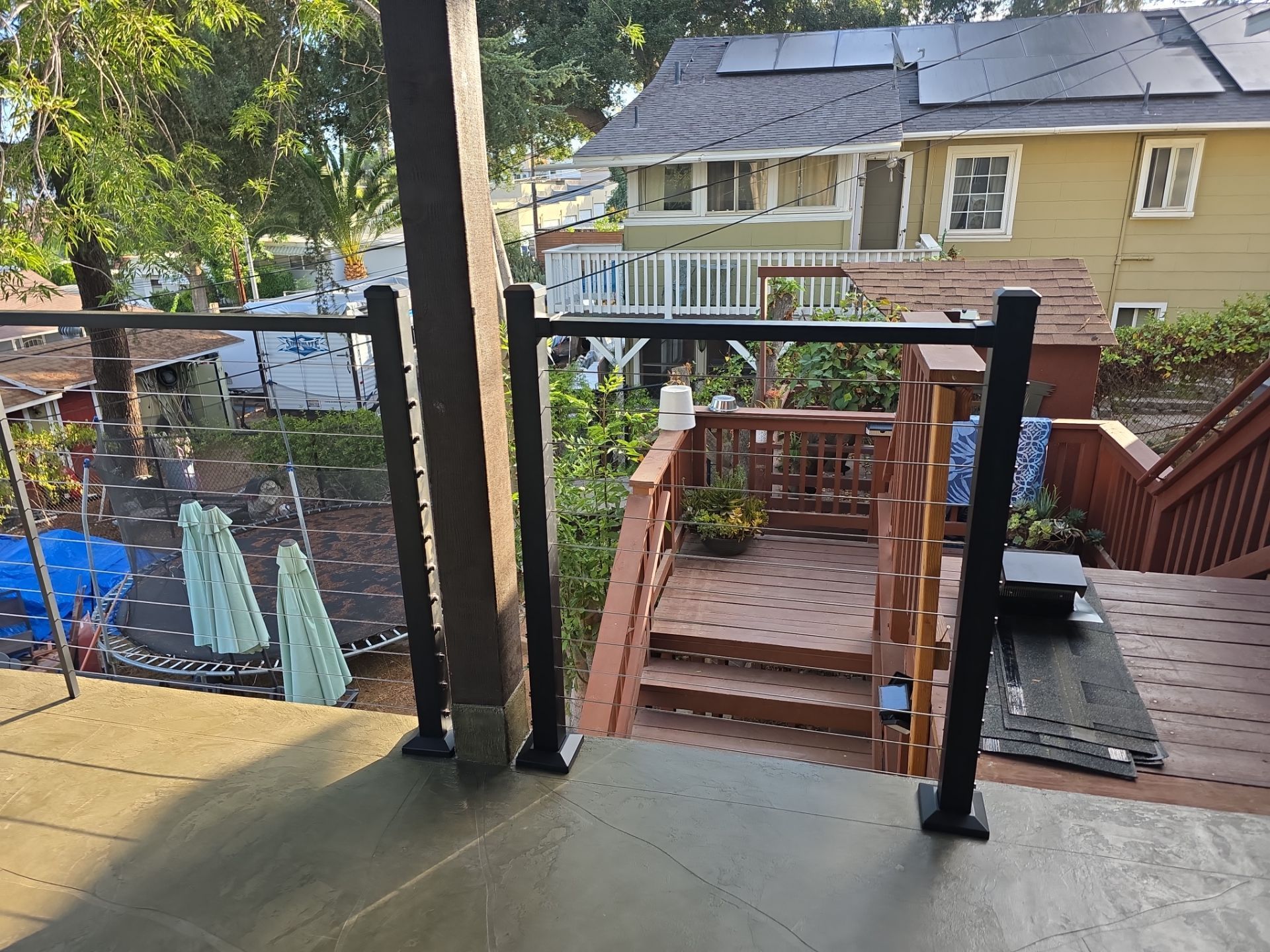 Wooden deck with glass railing, steps, and view of a backyard with a house in the background.