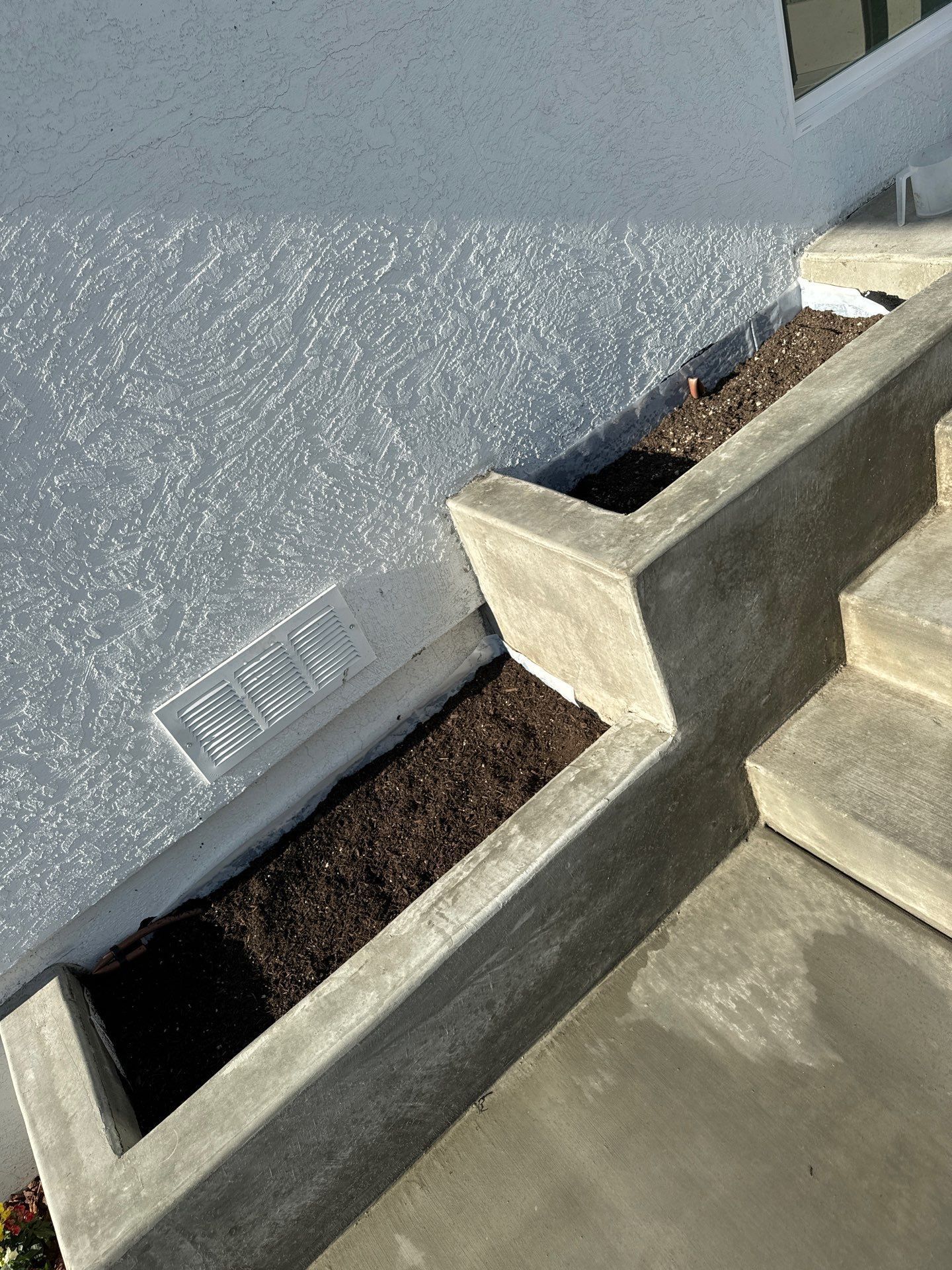 Concrete steps with built-in planters filled with dark soil along a light-colored stucco wall.