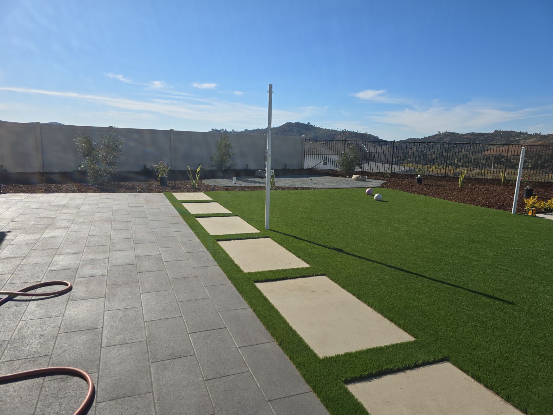 Patio with stepping stones leading to artificial grass lawn; blue sky and distant hills.