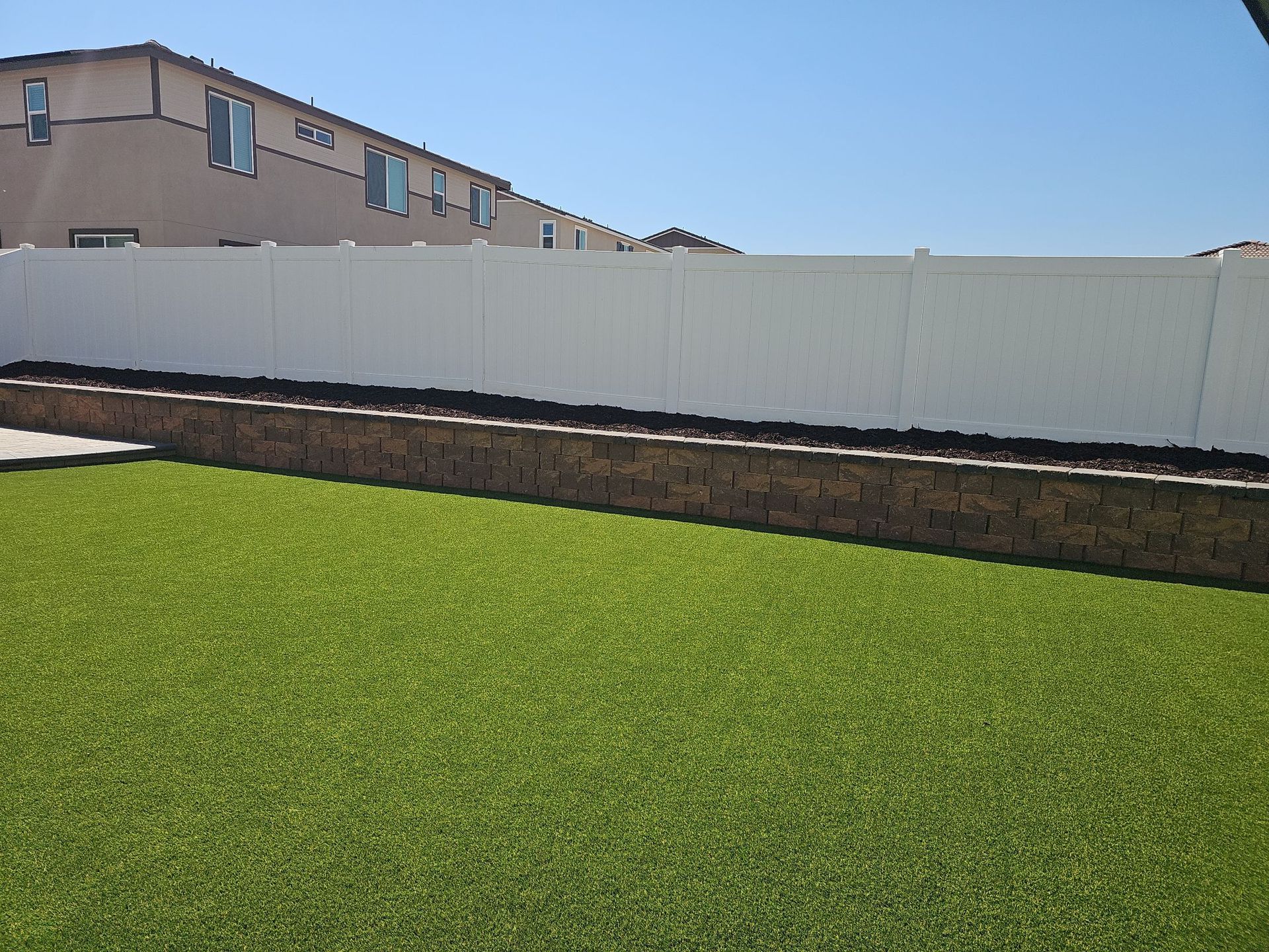 White fence atop a brick retaining wall and green lawn with buildings in background.
