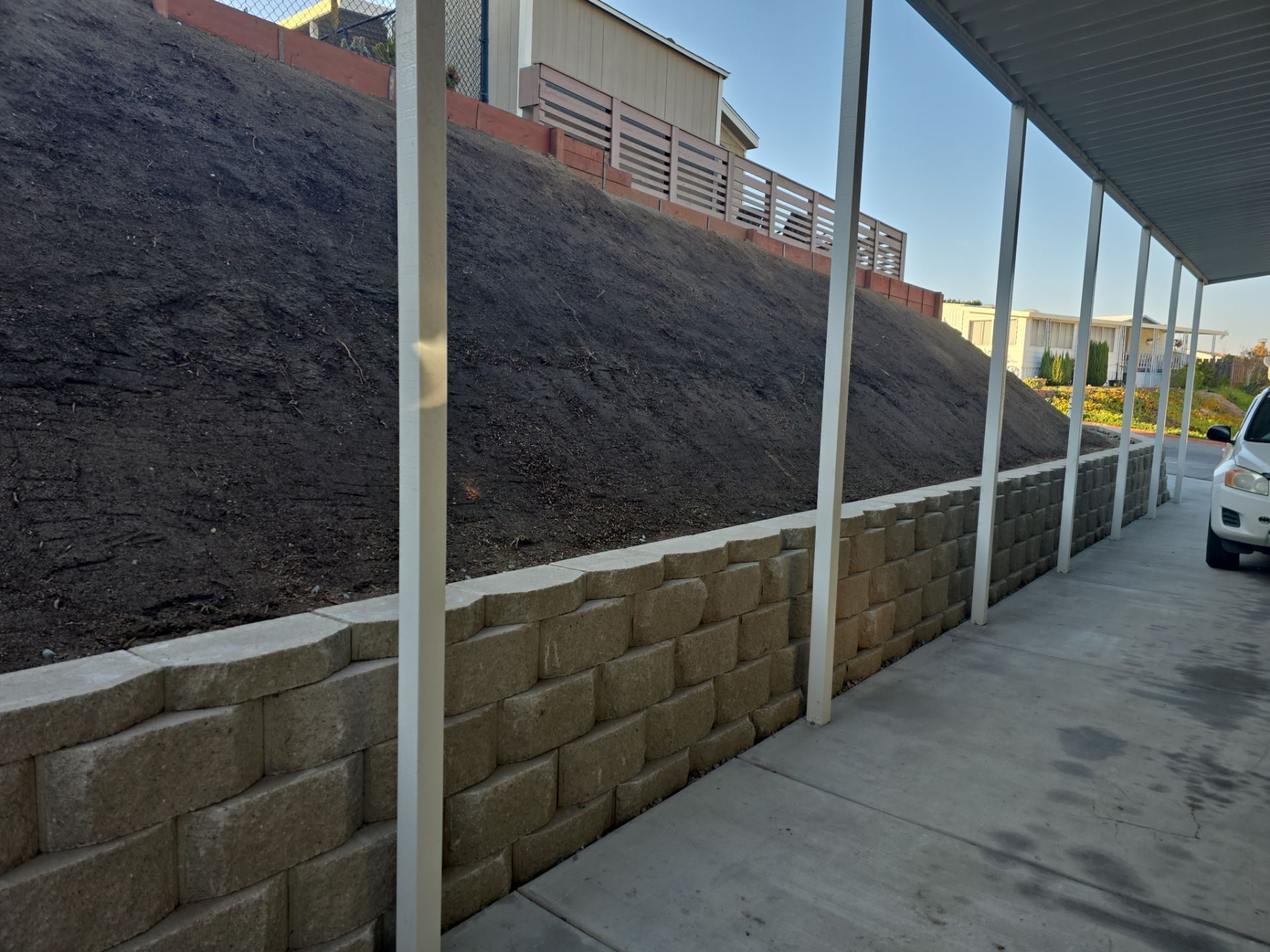 Retaining wall with dirt hillside and carport structure.
