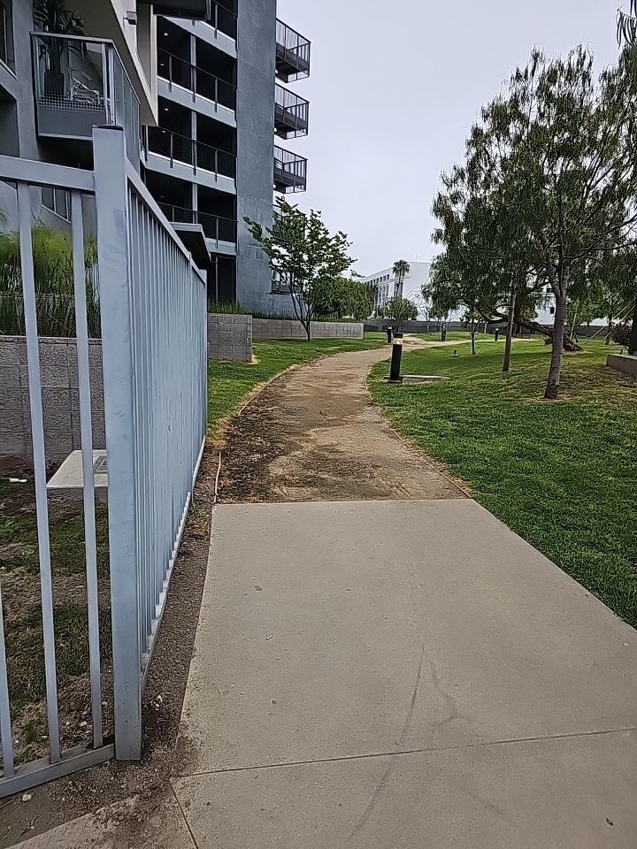 Gray metal fence and concrete path leading to a grassy area, with apartment building in the background.