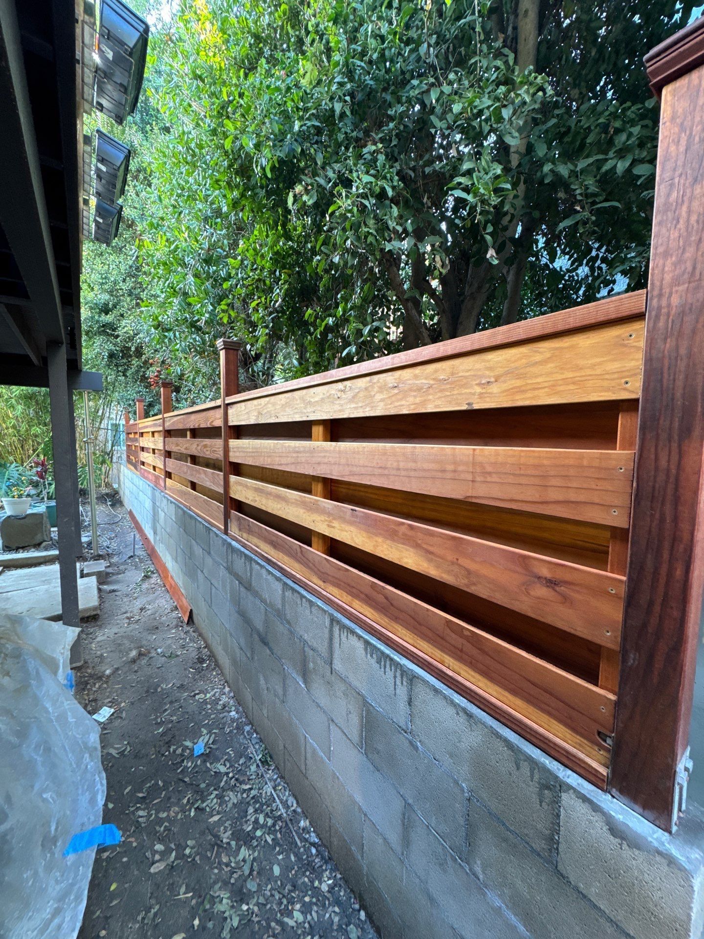 Wooden fence on a concrete block wall next to a lush green hillside.