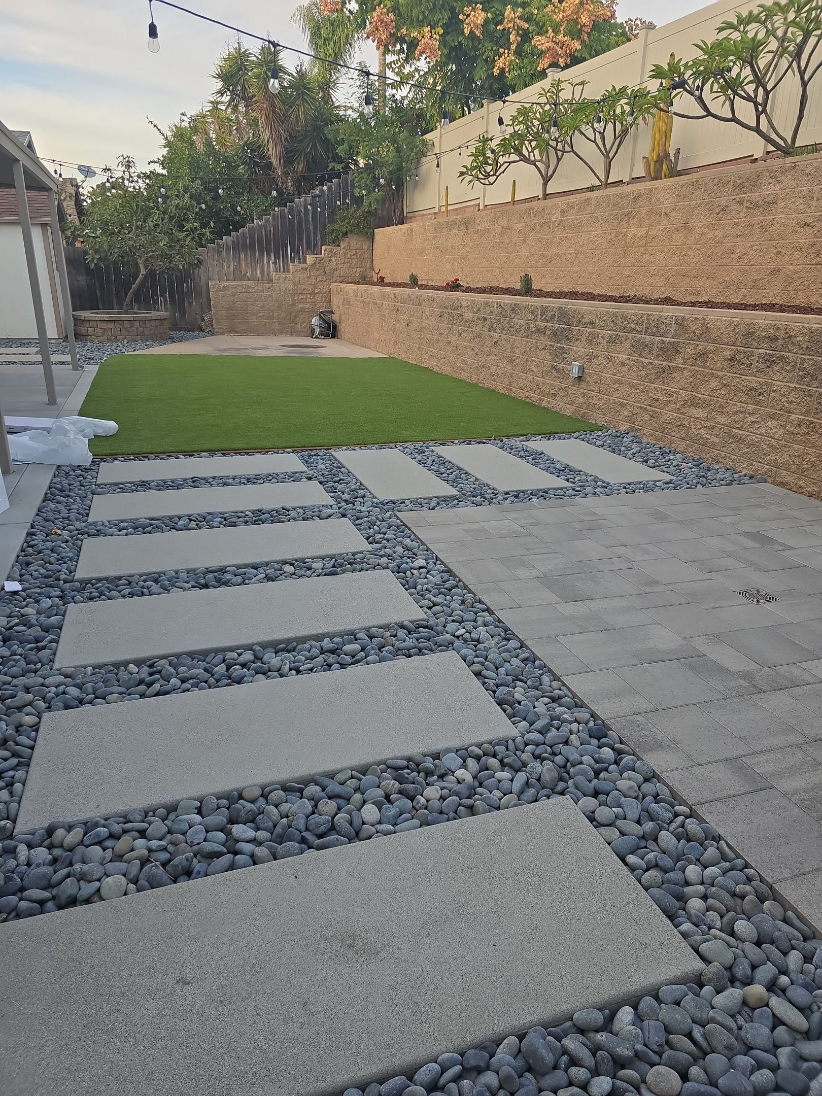 Stone path with rectangular pavers and dark rocks leading to a grassy area and terraced wall.