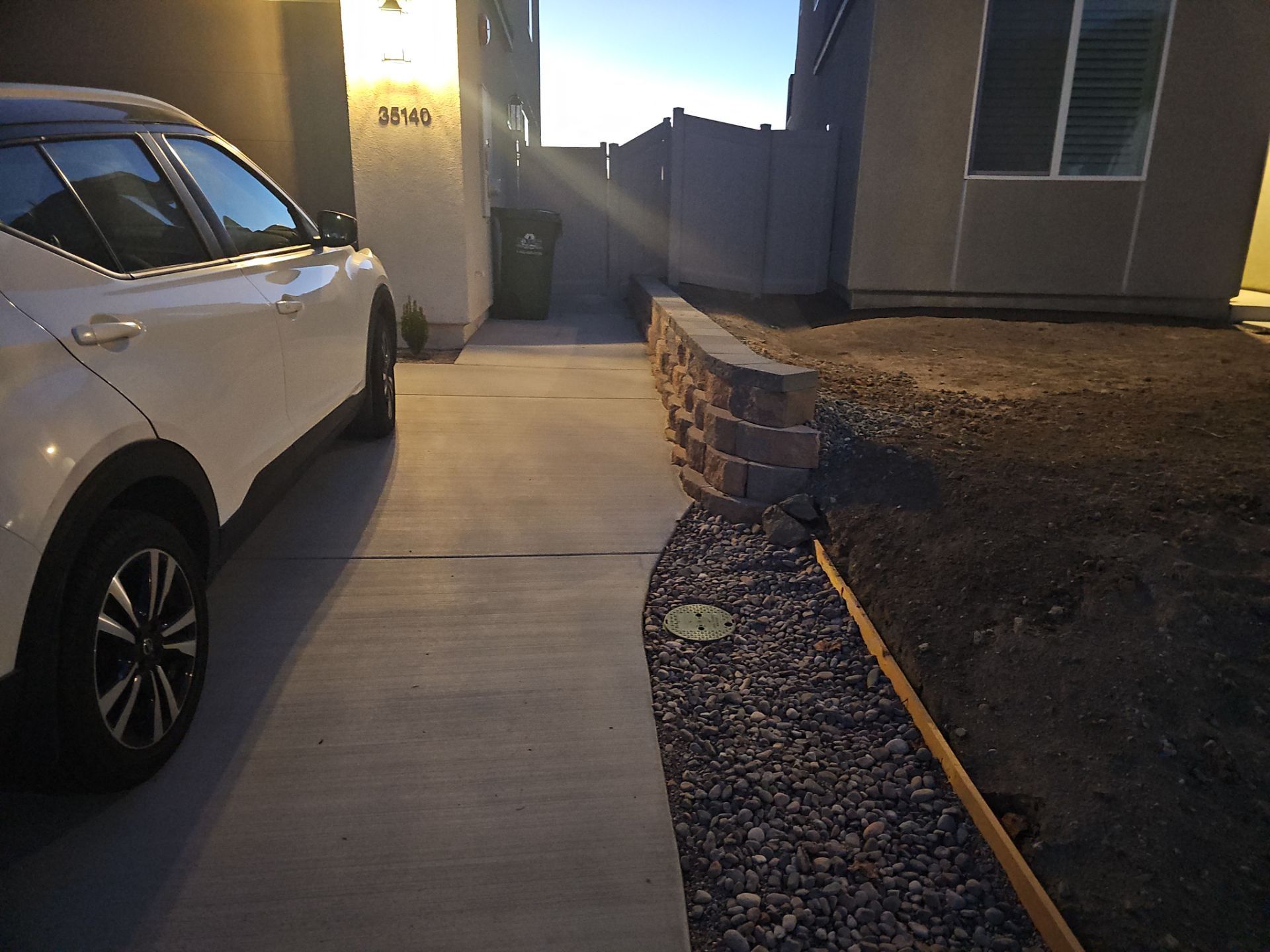 White SUV parked on a concrete driveway next to a landscaped yard with a retaining wall.