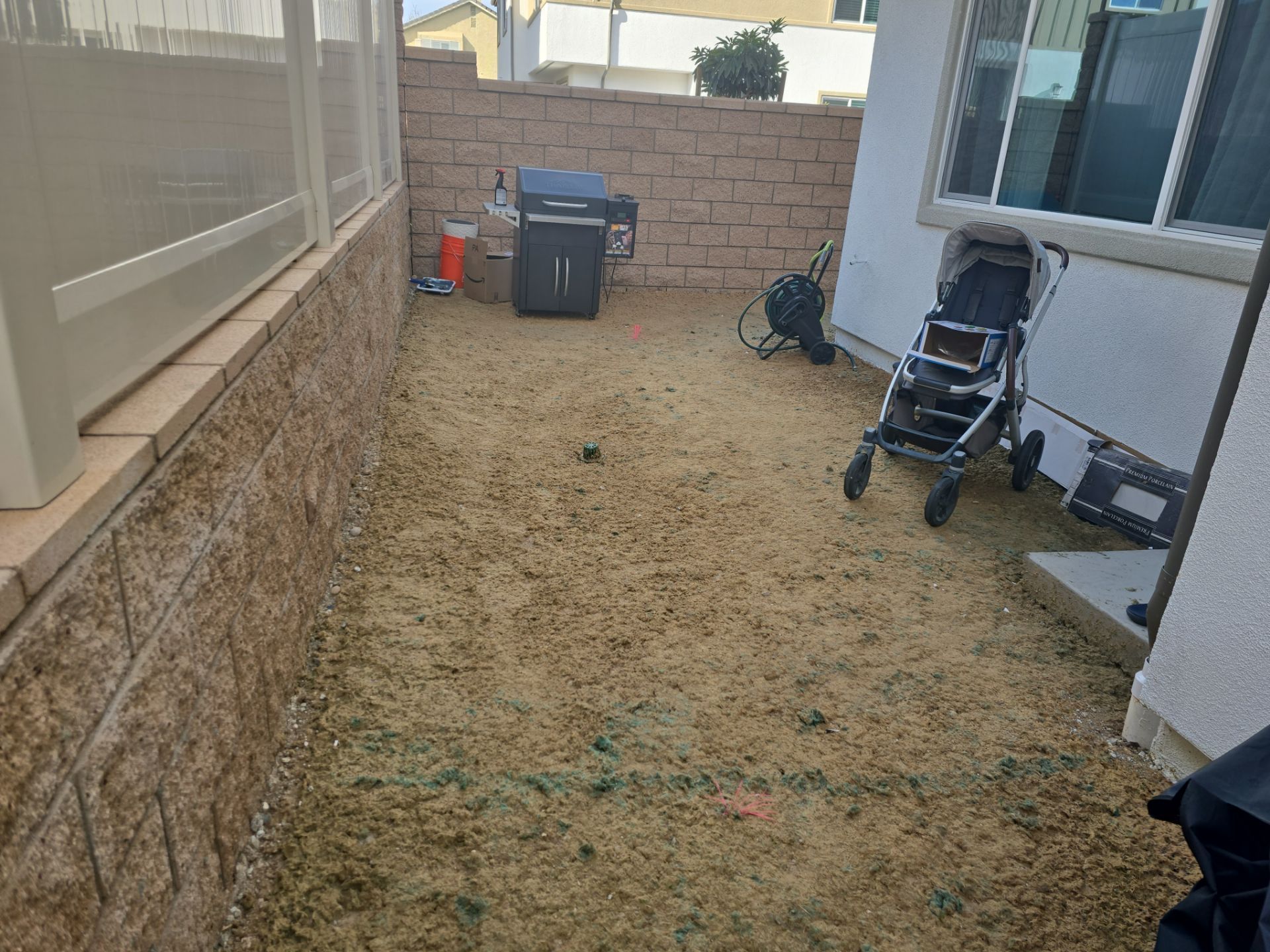 Backyard with a grill, stroller, and brick wall. Dry, dirt ground.