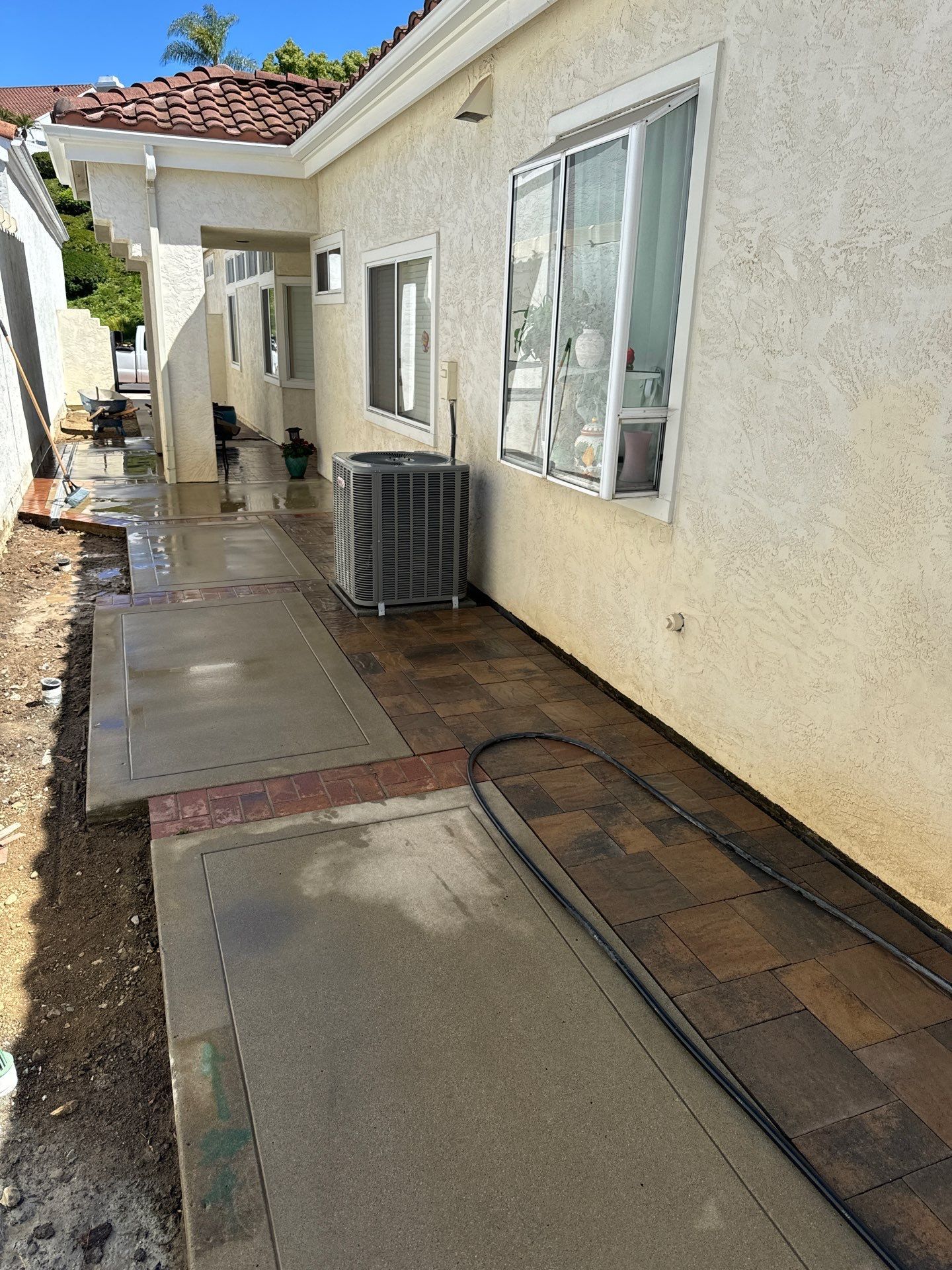 Exterior of a building with a concrete and brick walkway, air conditioning unit, and garden bed.