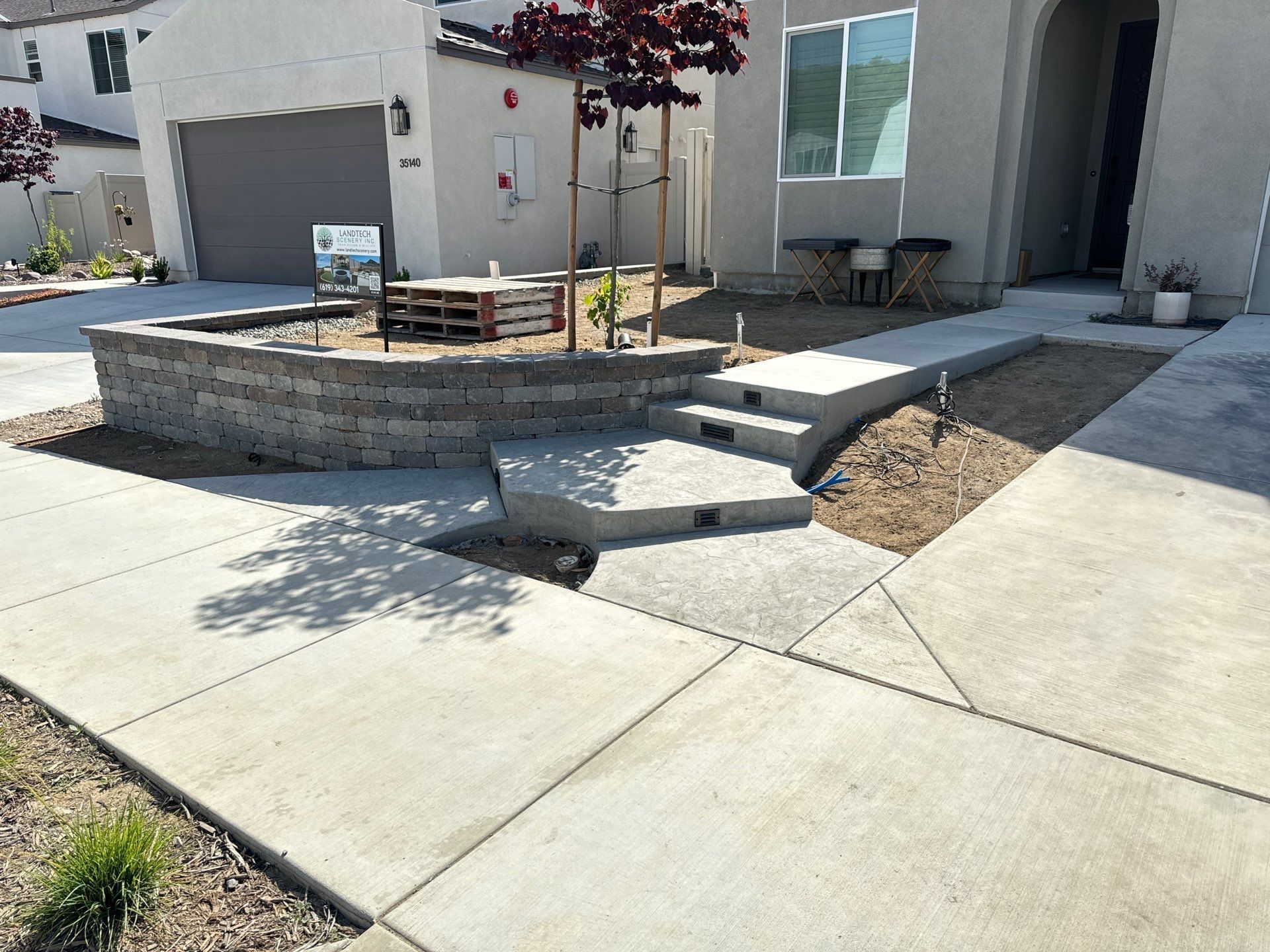 Front yard with concrete walkway, steps, and retaining wall. Small trees and gravel landscaping.