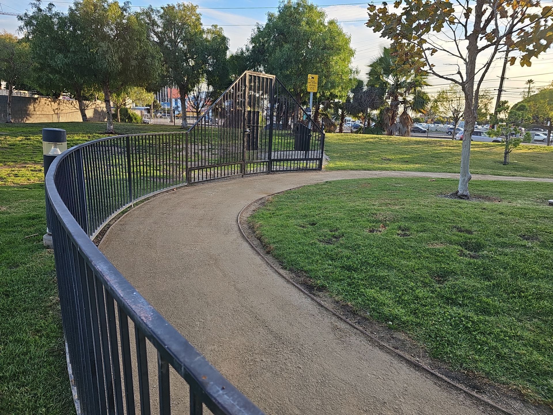 Curved gravel path with black railing in a park, leading to a playground in the background. Green grass and trees.
