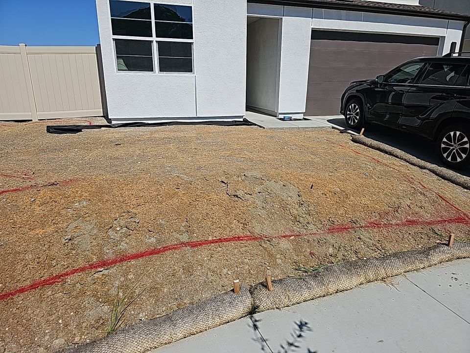 Front yard with brown gravel, red lines, and a house with a garage and a car.