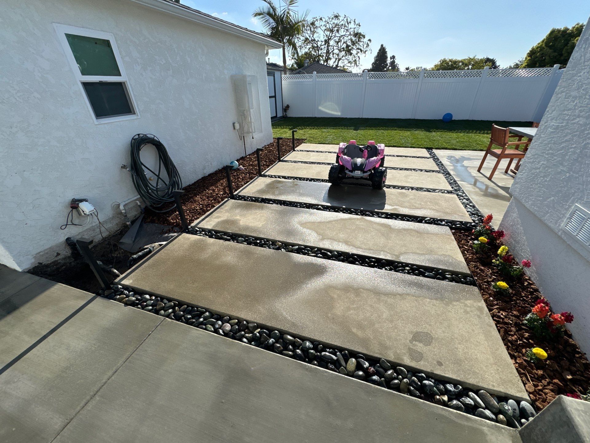 Backyard patio with concrete pavers, black rocks, and a pink toy car.