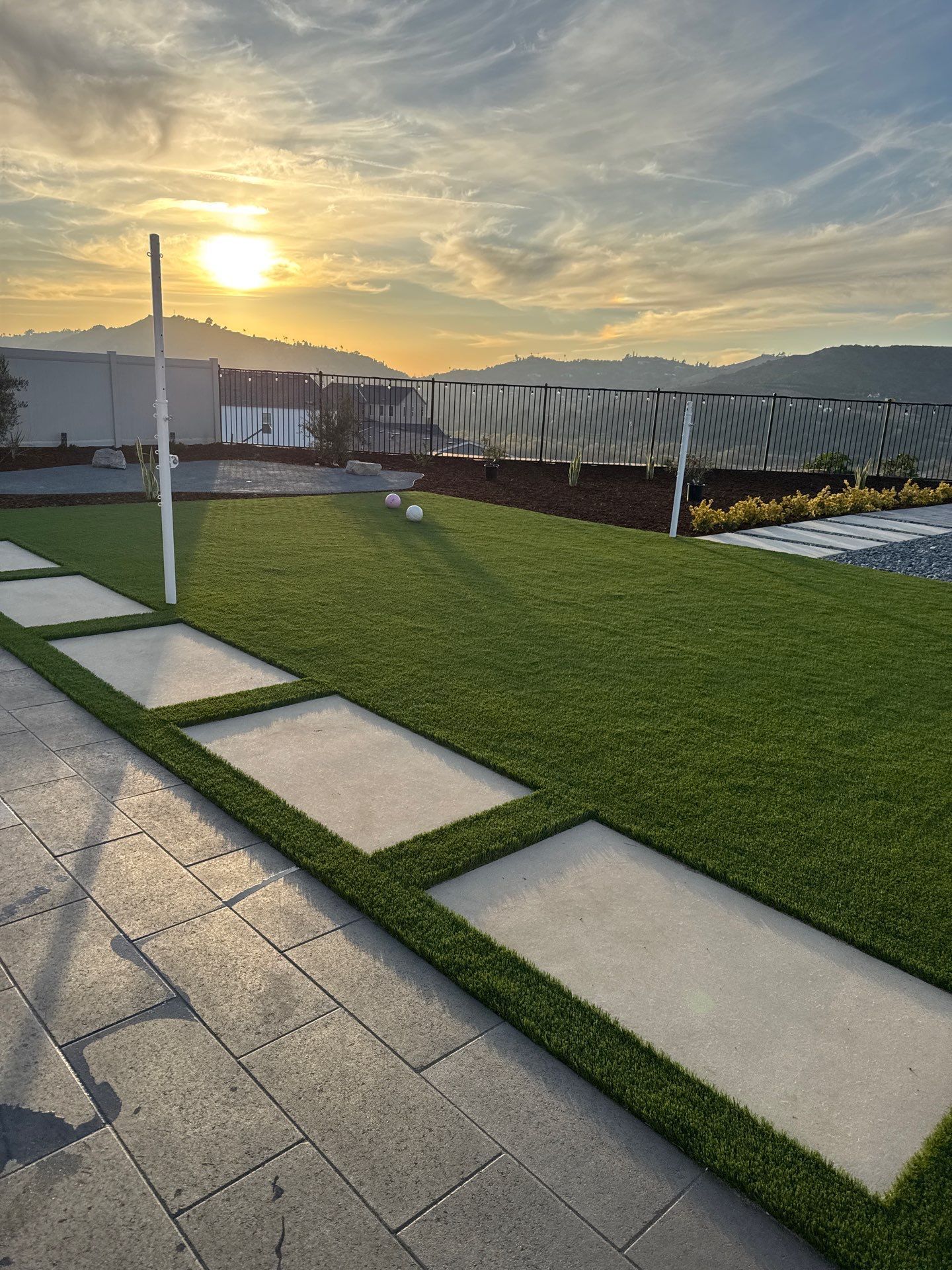 Sunset over a green lawn with square stepping stones. Mountains in the background.
