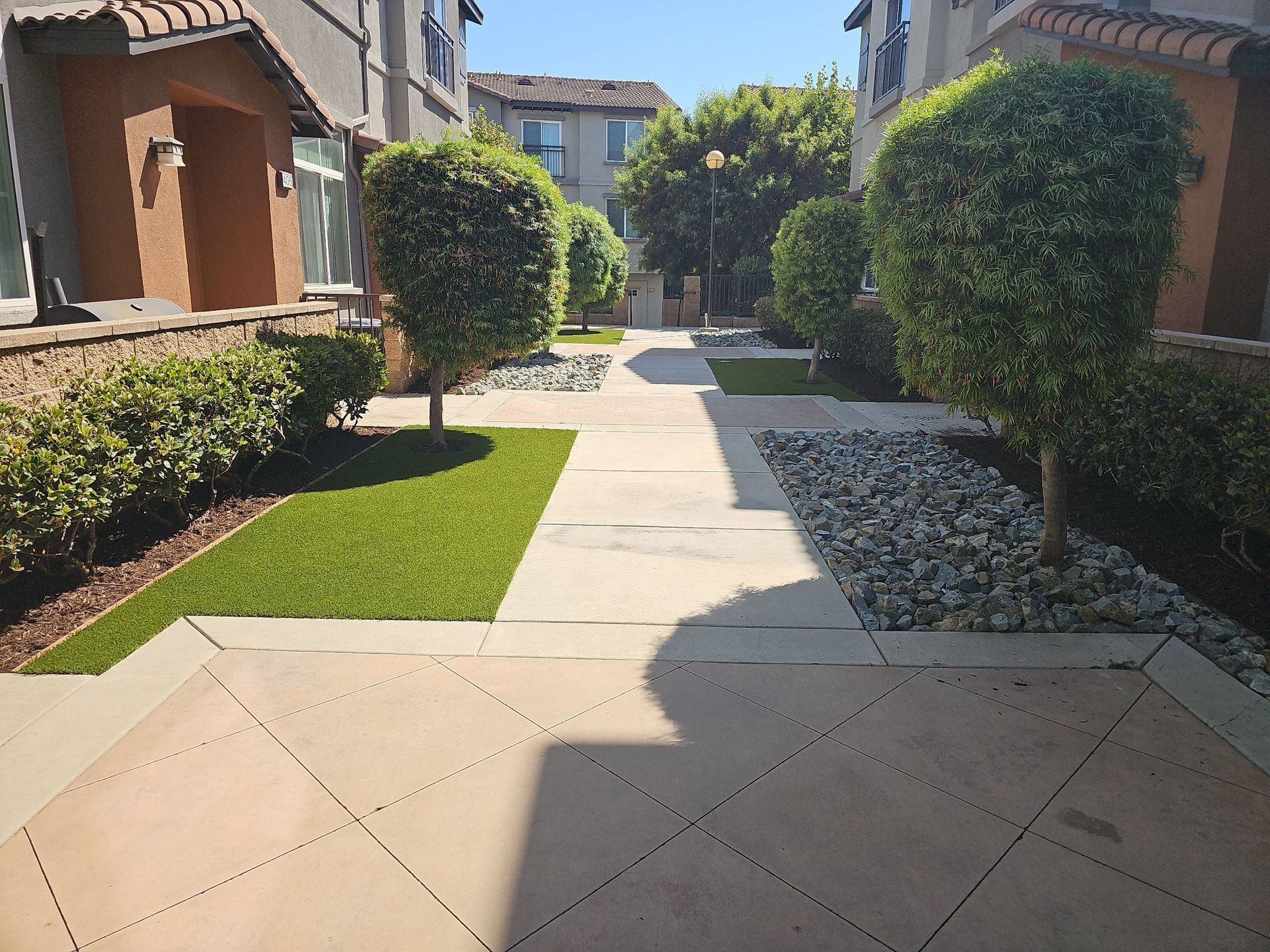 Courtyard with concrete walkways, artificial turf, and trimmed bushes between townhouses.