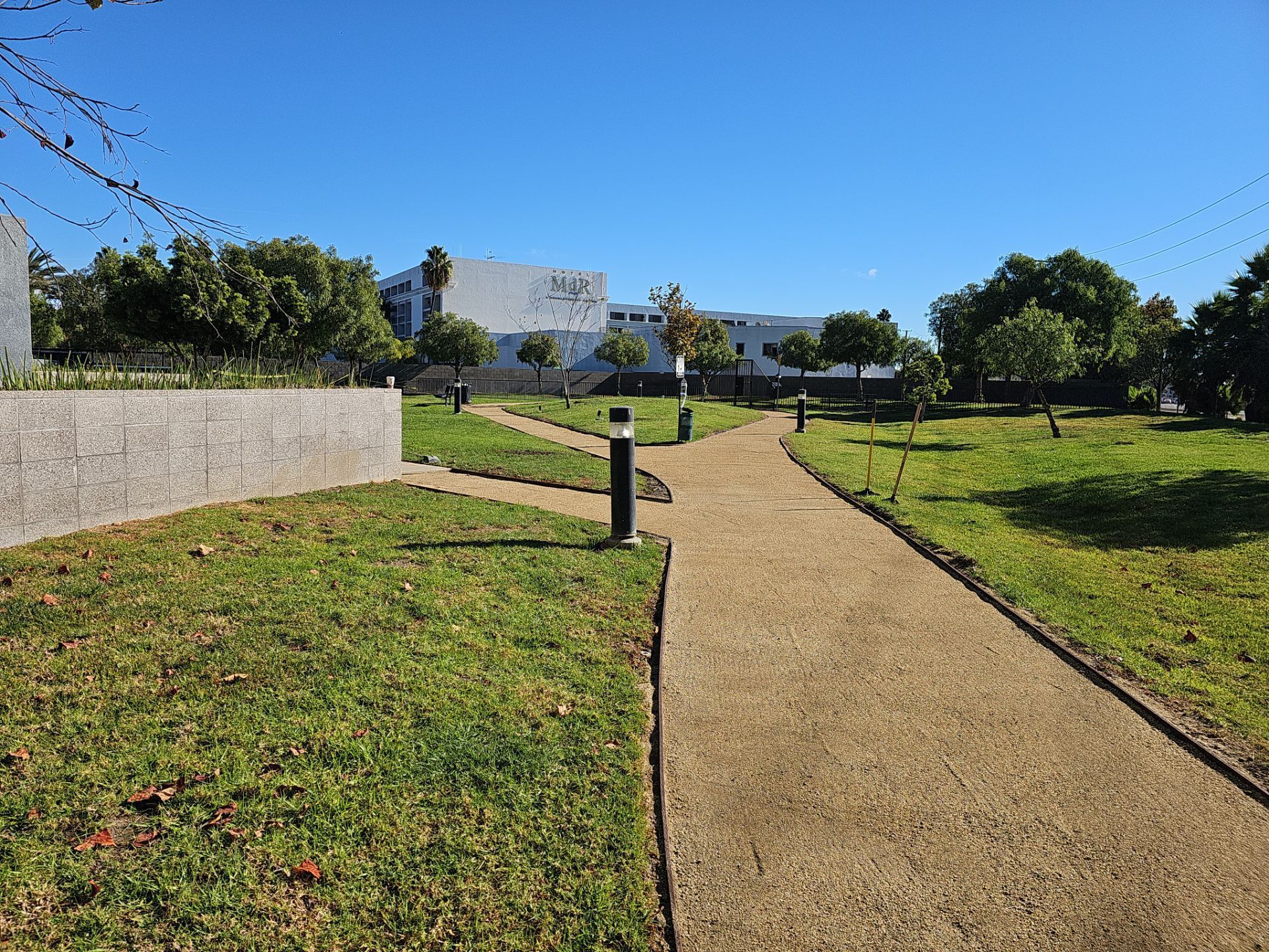 Park with paved paths, grass, trees, and buildings against a clear blue sky.