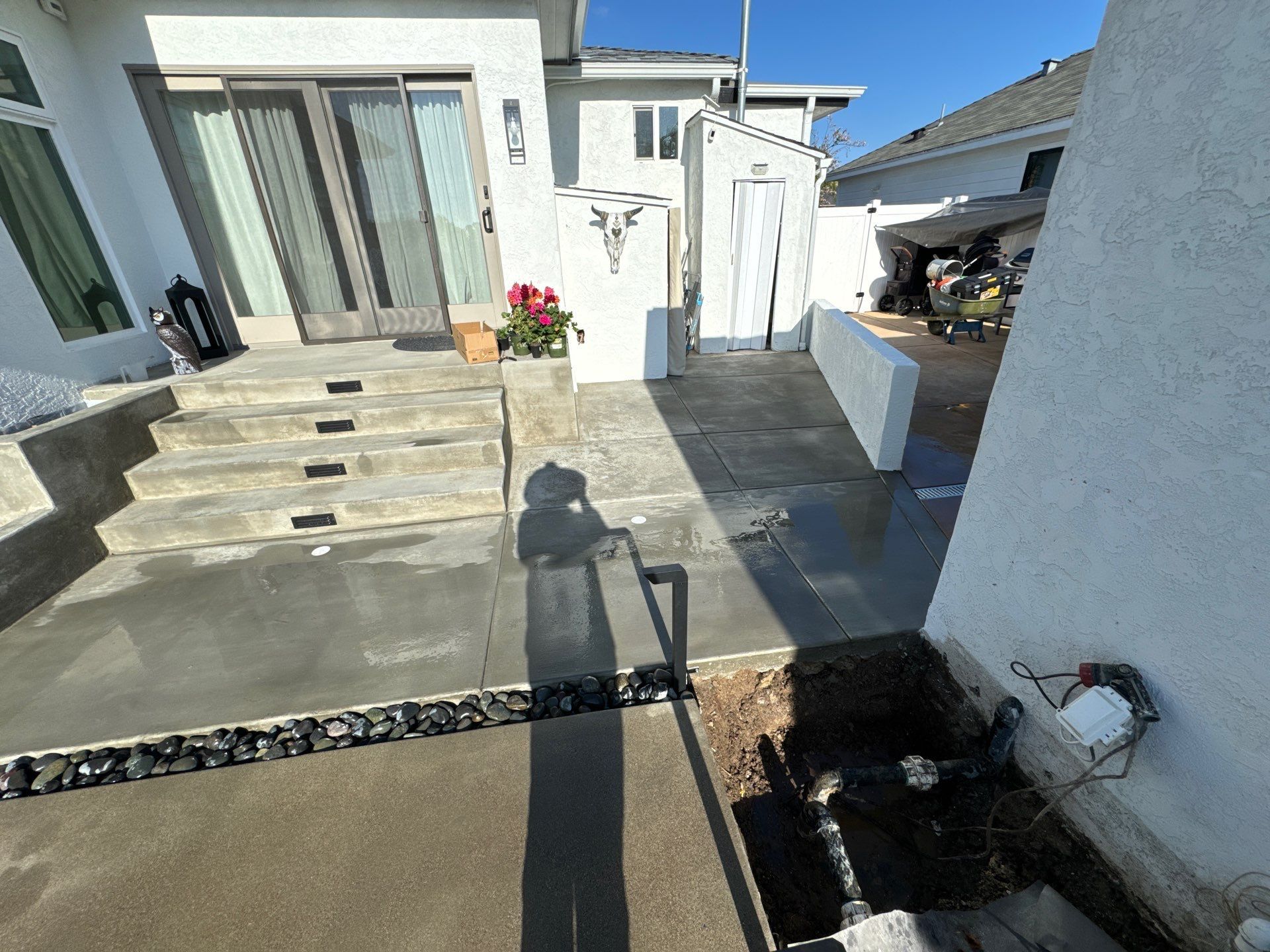 Concrete patio with steps, drainage, and a partially open door to the house; sunny day.