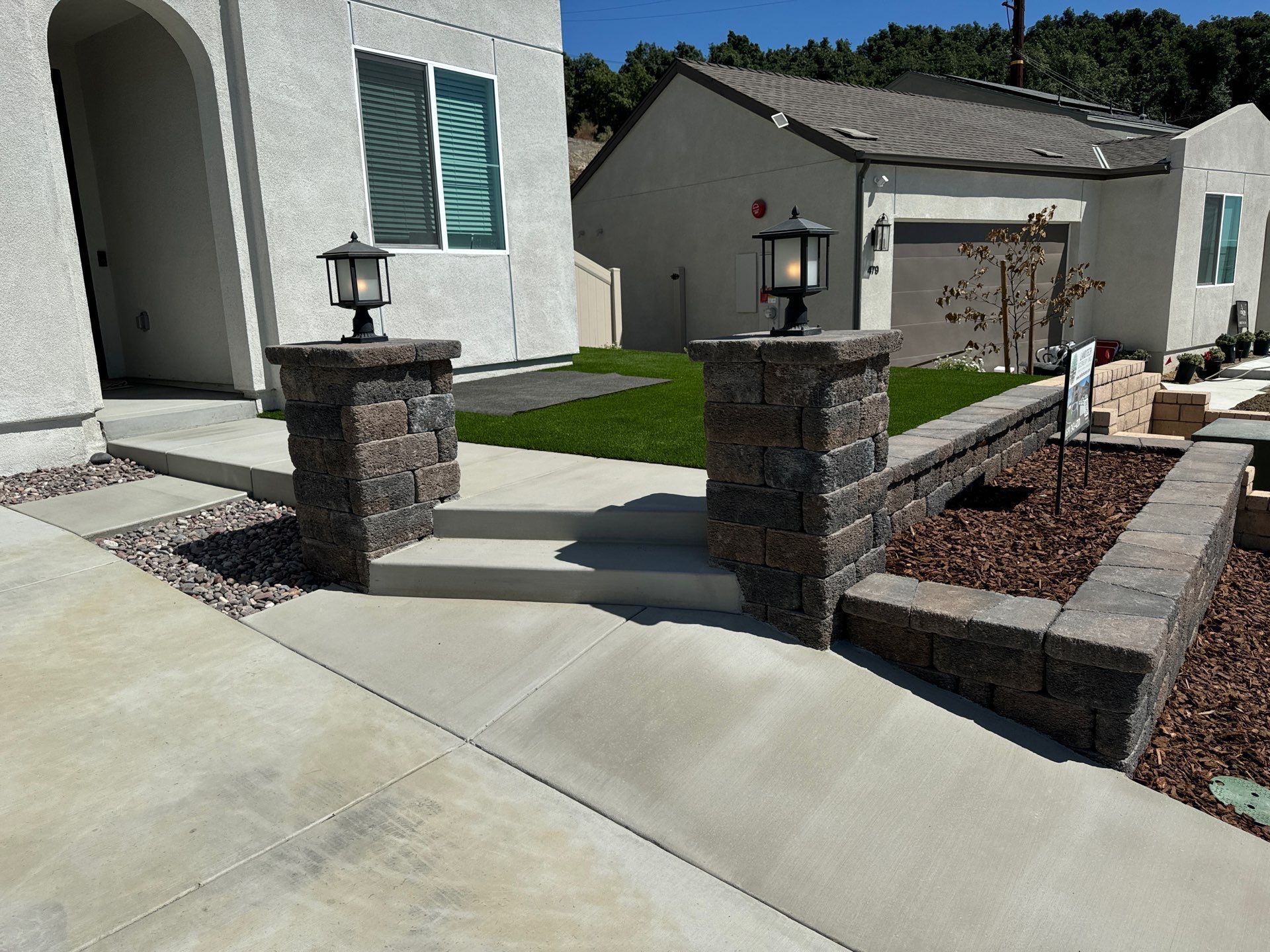 Concrete steps lead to a house entrance. Brick pillars with lanterns flank the steps.