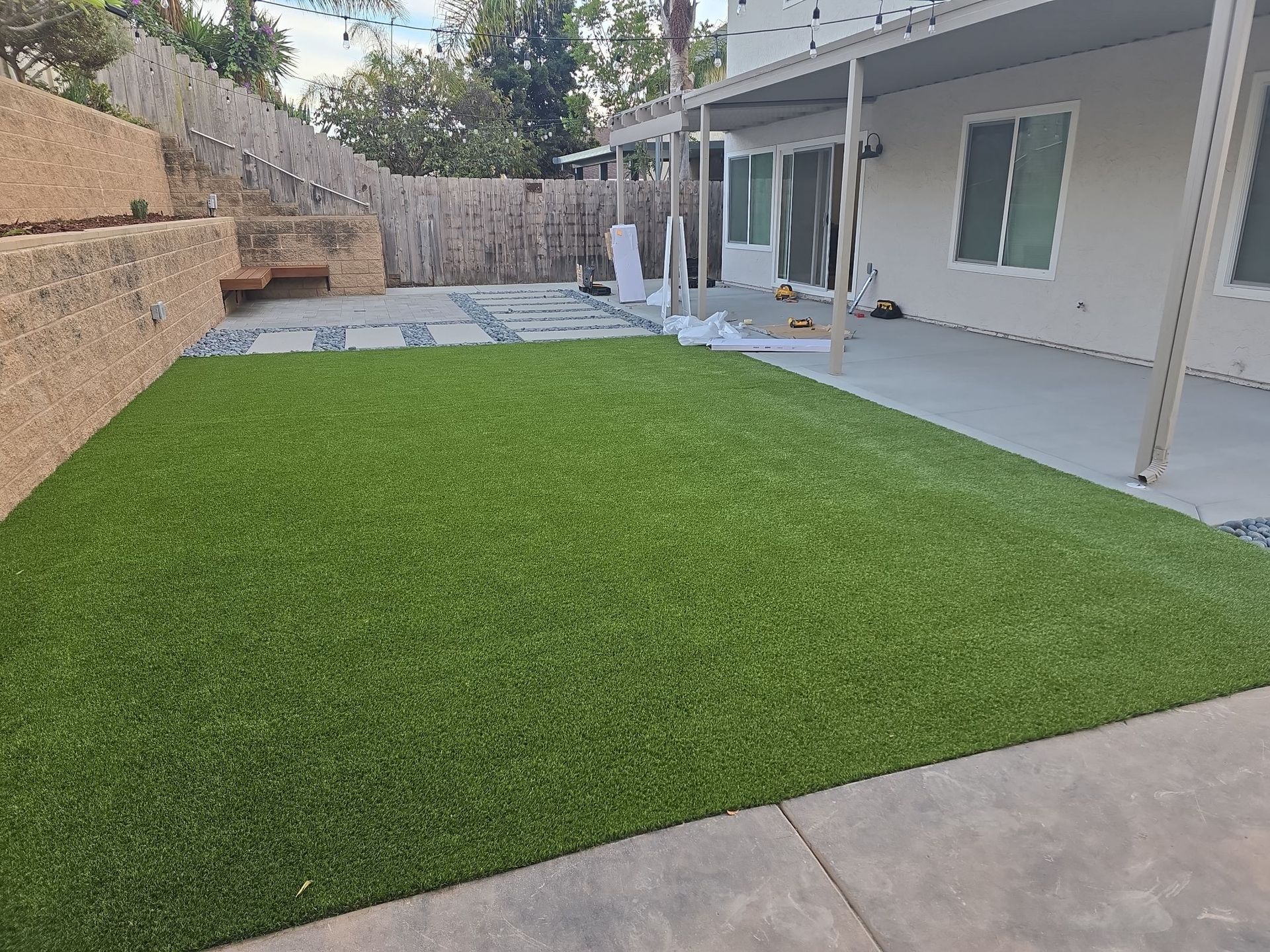 Green artificial turf in a backyard with a patio, concrete retaining wall, and house.