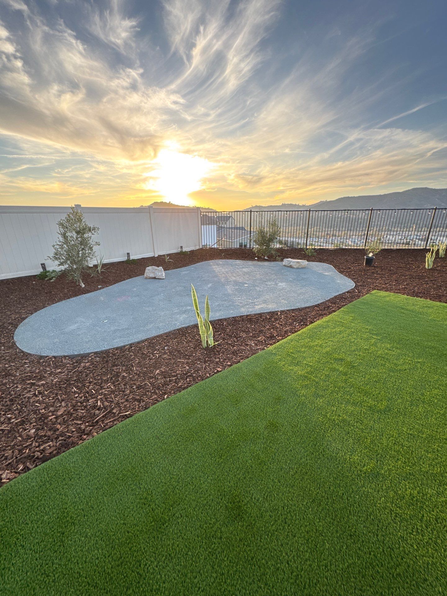 Sunset over landscaped backyard with gravel, wood chips, and artificial grass.