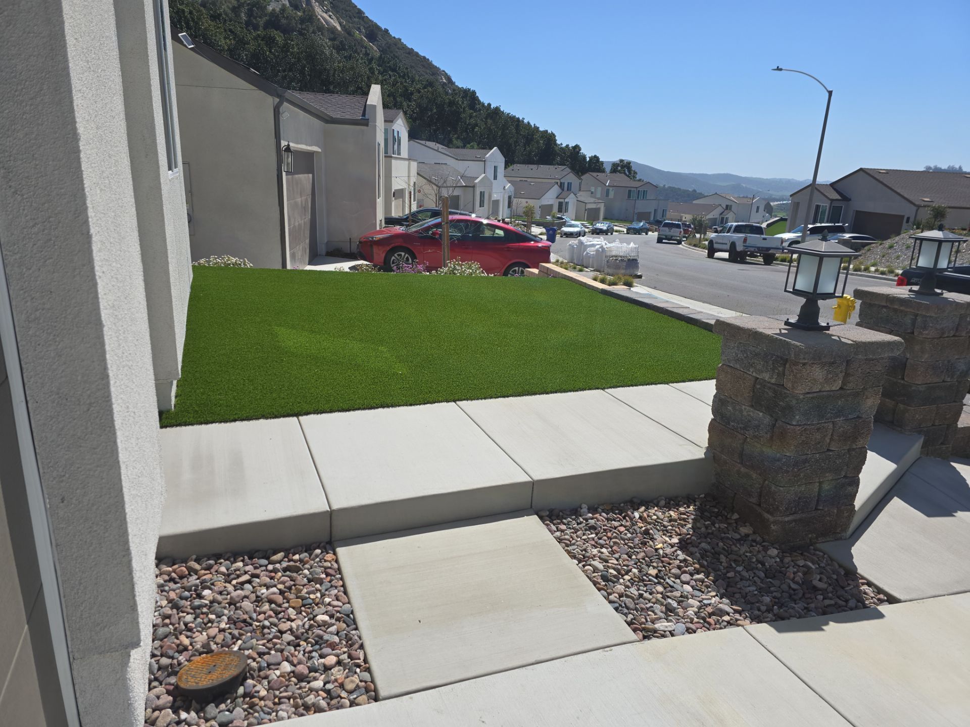 A red car parked on a lawn with green grass, concrete sidewalk, and a street in a suburban neighborhood.