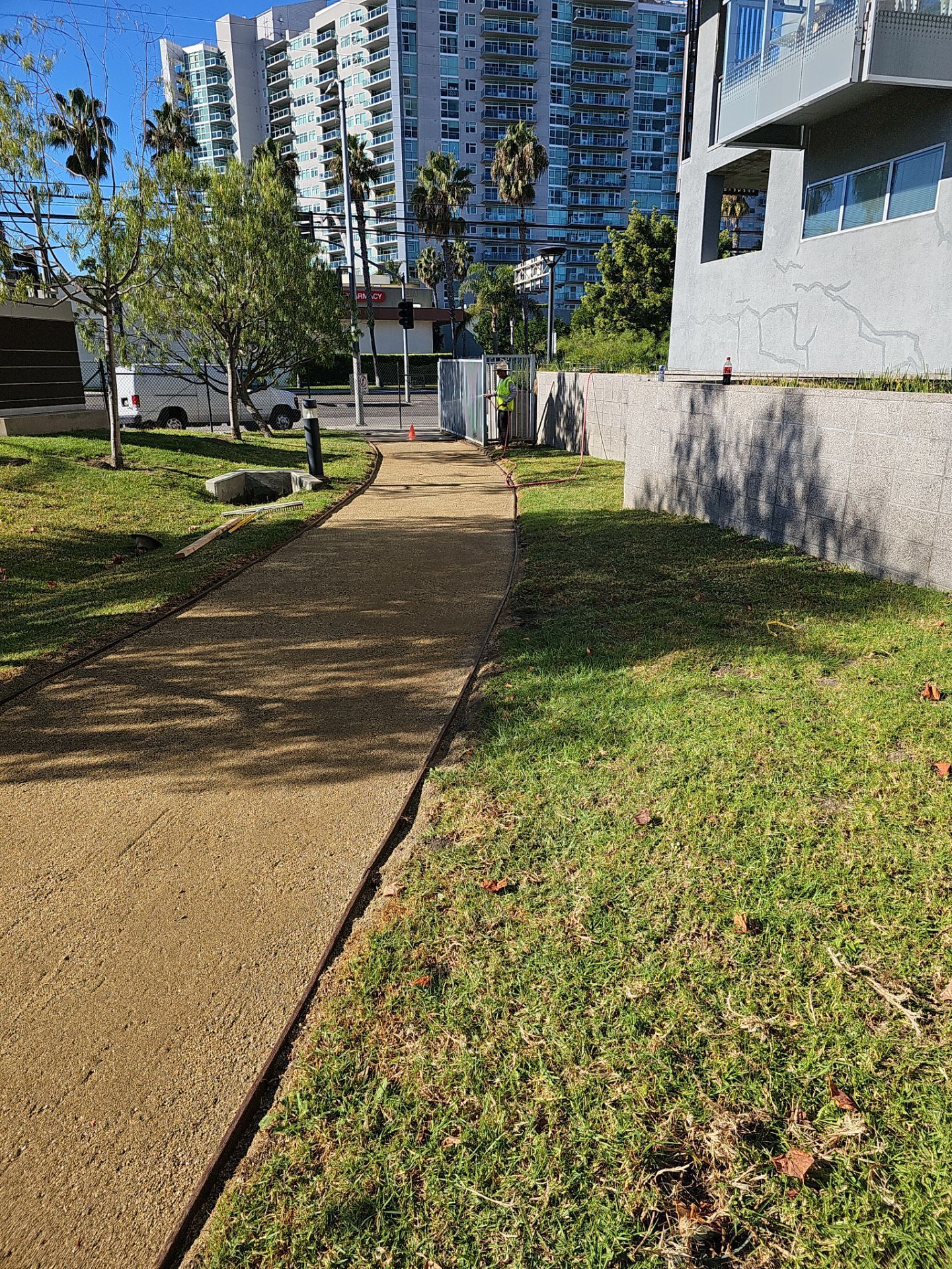 A gravel path leads to a gate, bordered by grass and a low wall, with a tall building in the background.