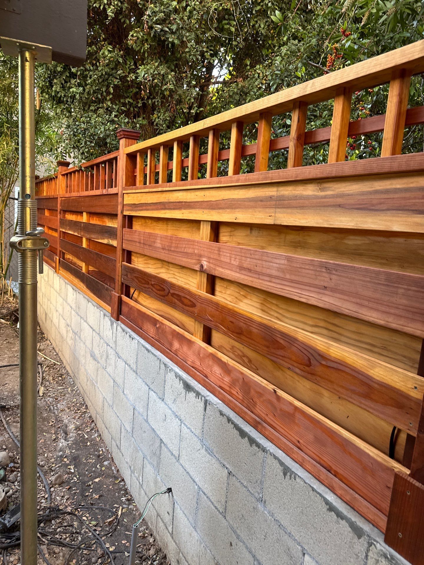 A wooden fence with a dark reddish-brown top rail and horizontal planks, built on a cinder block base.